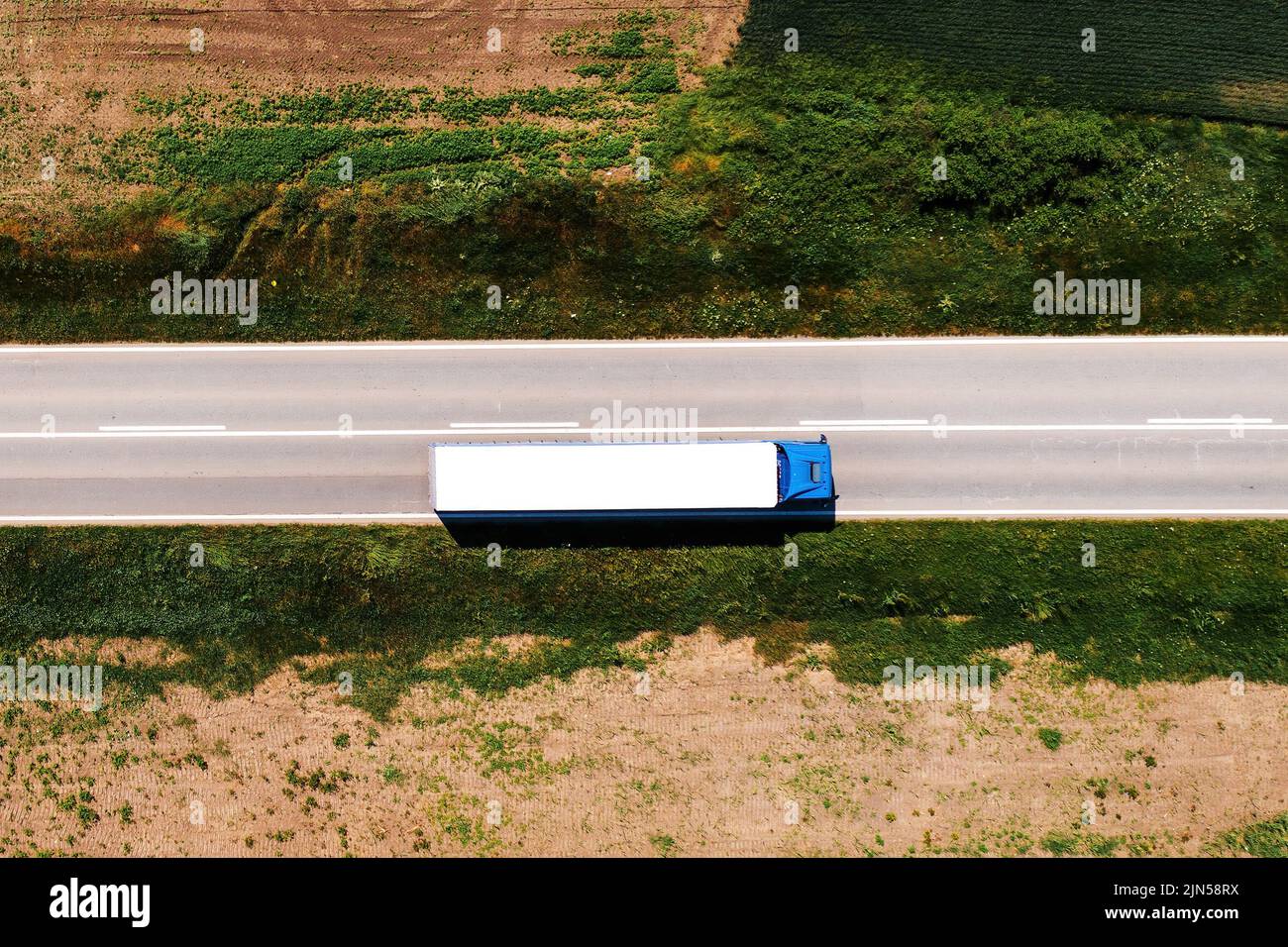 Photo aérienne de semi-camion conduisant le long de l'autoroute à travers le paysage de campagne, drone pov directement au-dessus le jour ensoleillé de printemps. Transport et lo Banque D'Images