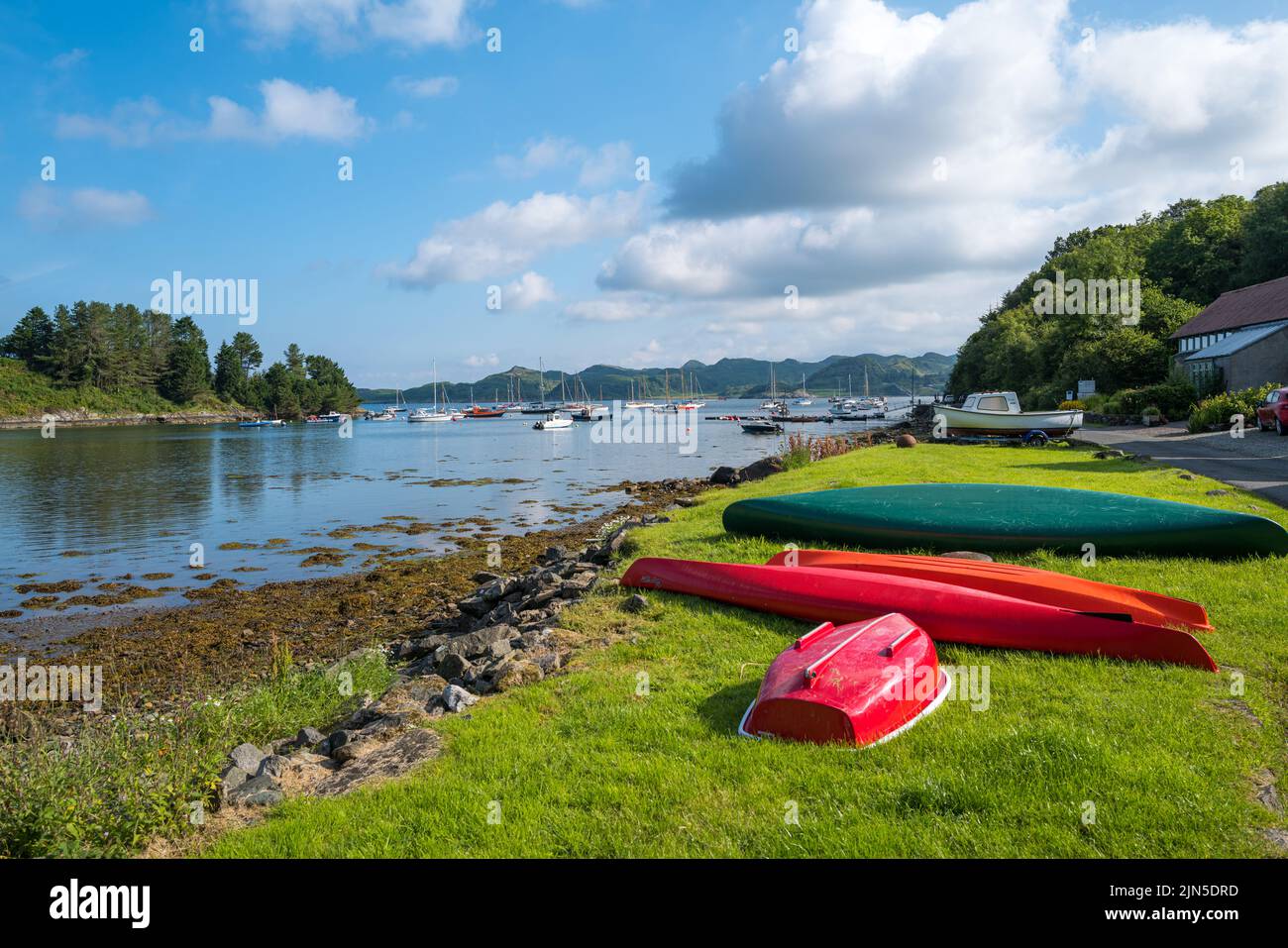 Kayaks en attente sur le côté du loch au port de Crinan Argyll Ecosse près du port et des bateaux amarrés dans la mer Banque D'Images