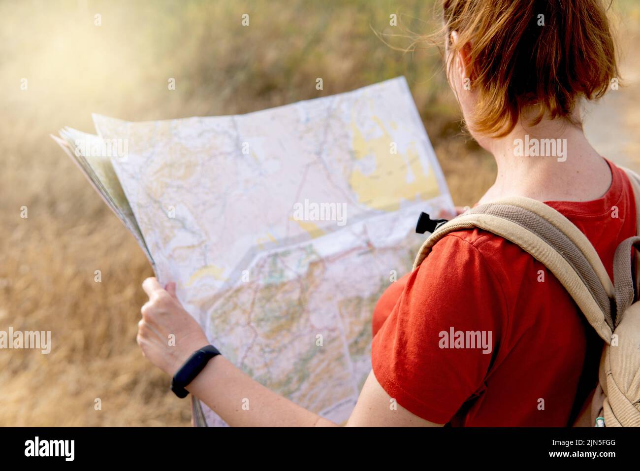Vue arrière d'une femme dans un t-shirt orange avec un sac à dos regardant une carte sur la nature, la liberté, le voyage et les concepts de bien-être Banque D'Images
