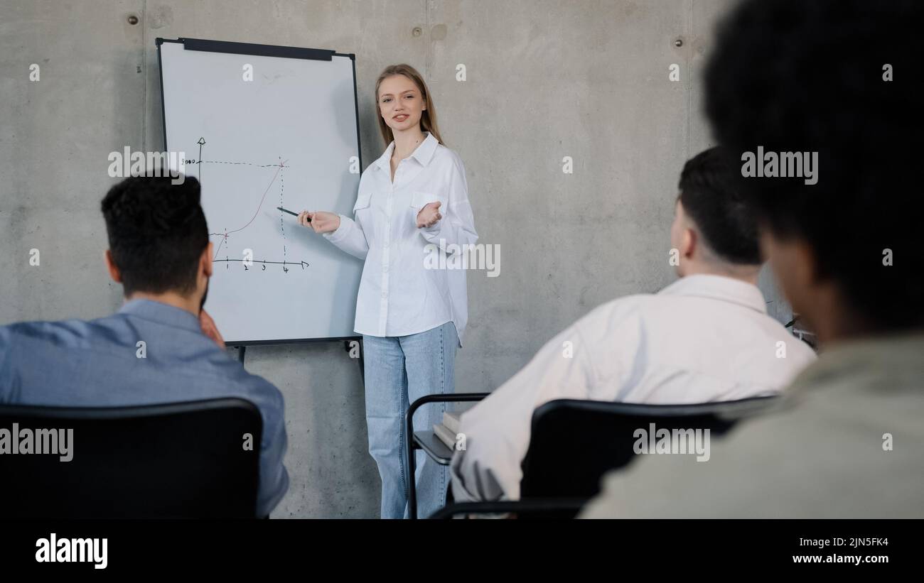 Une jeune femme enseignante se tient près du tableau de conférence en classe à la leçon explique le plan de travail raconte un nouveau sujet une fille caucasienne tuteur pose la question diverse Banque D'Images