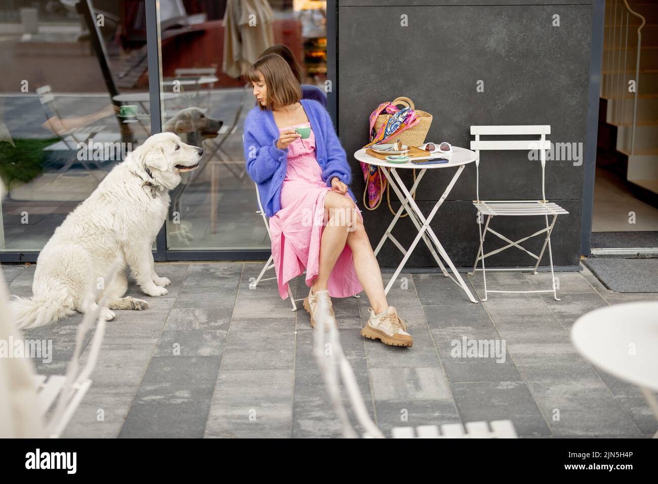 Elle est assise avec son adorable chien blanc au café dans une rue Banque D'Images