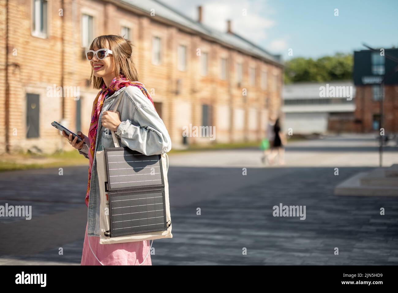 Une femme charge le téléphone depuis un panneau solaire portable tout en marchant à l'extérieur Banque D'Images