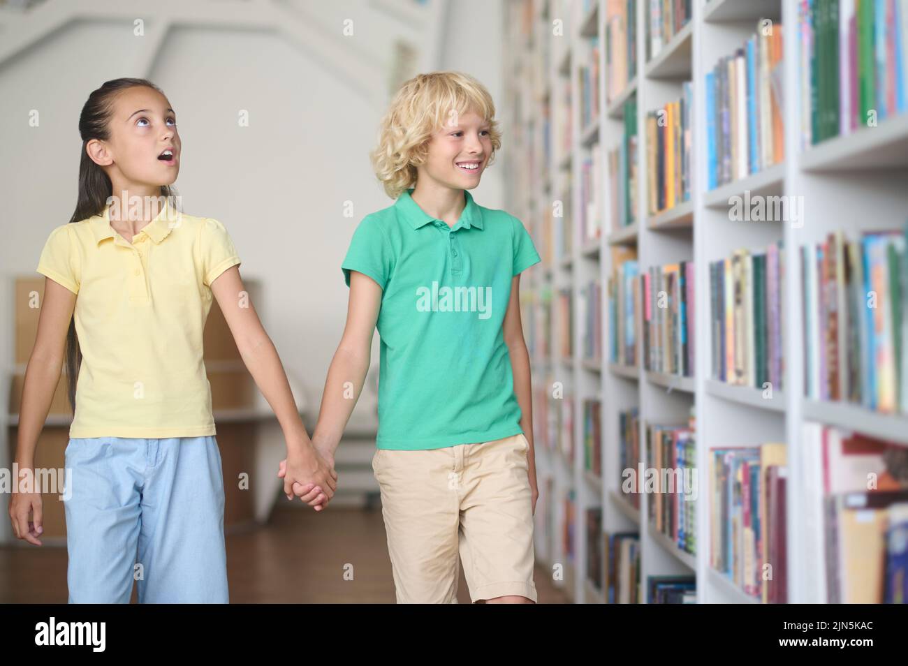 Deux enfants regardent les étagères empilées avec des livres Banque D'Images