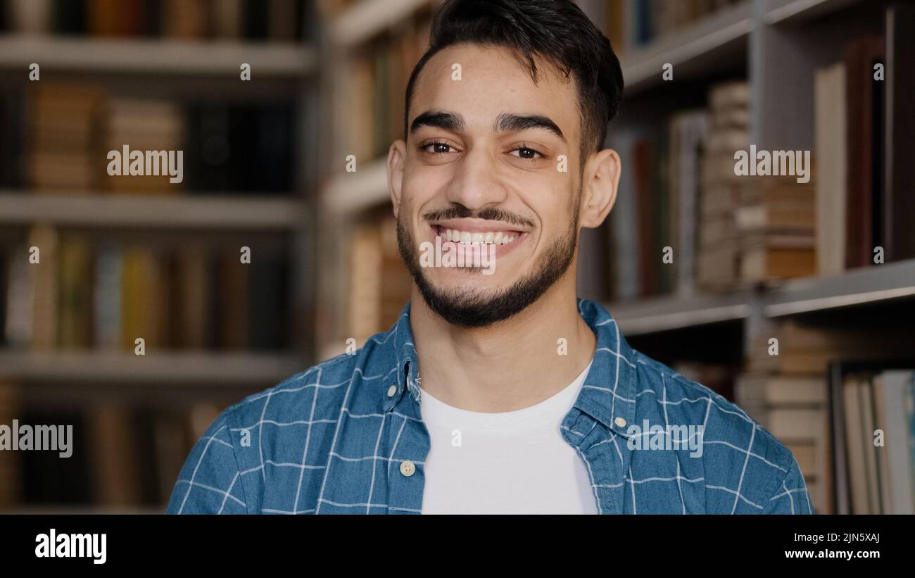 Gros plan portrait masculin jeune beau heureux homme debout dans la bibliothèque regardant l'appareil photo sourire un sourire sain et touffant les nodes tête dans l'approbation Banque D'Images