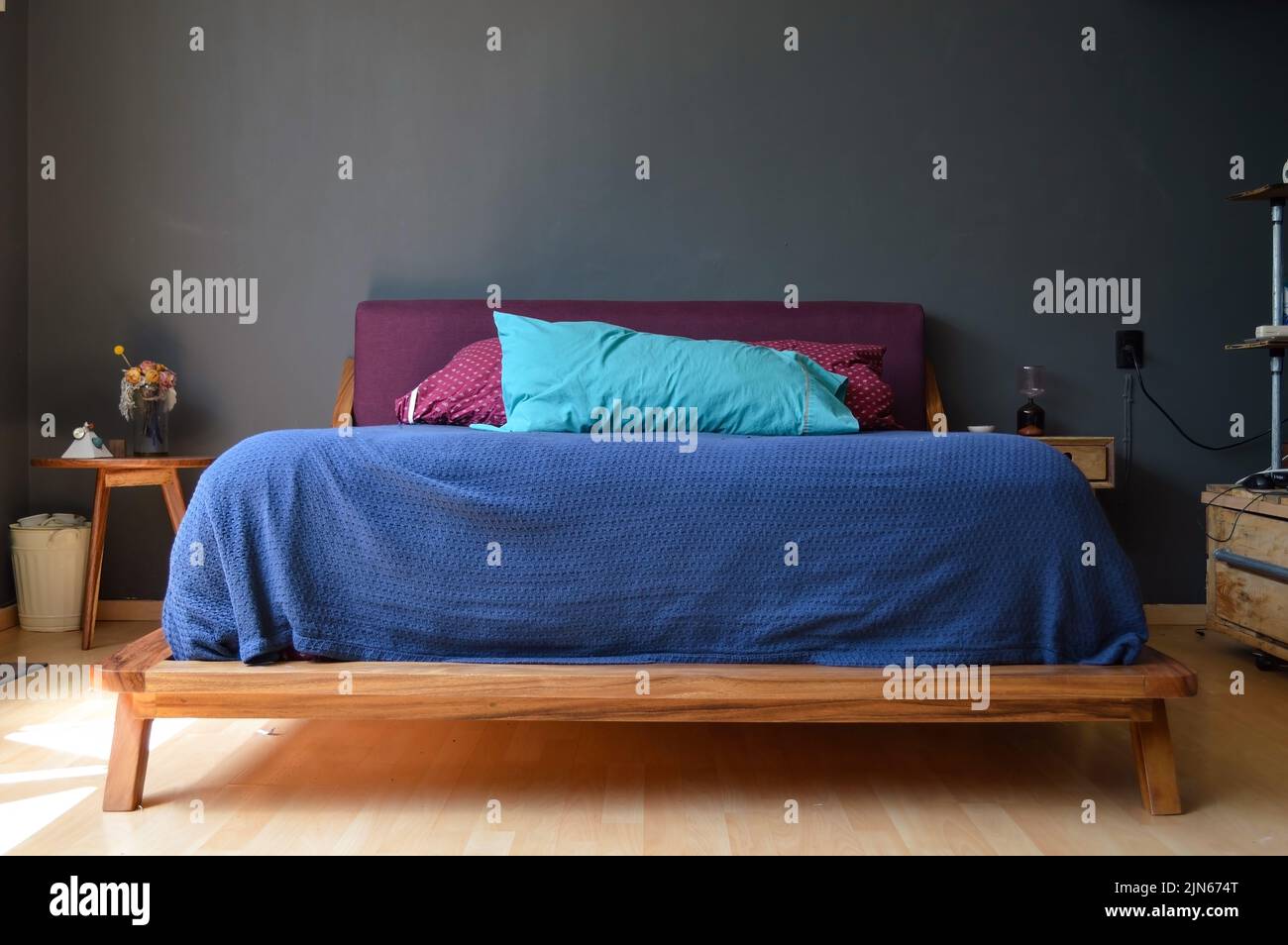 Cette chambre confortable dispose d''un élégant lit bleu et rouge et d''une crédence en bois de chaque côté, contre le mur gris Banque D'Images