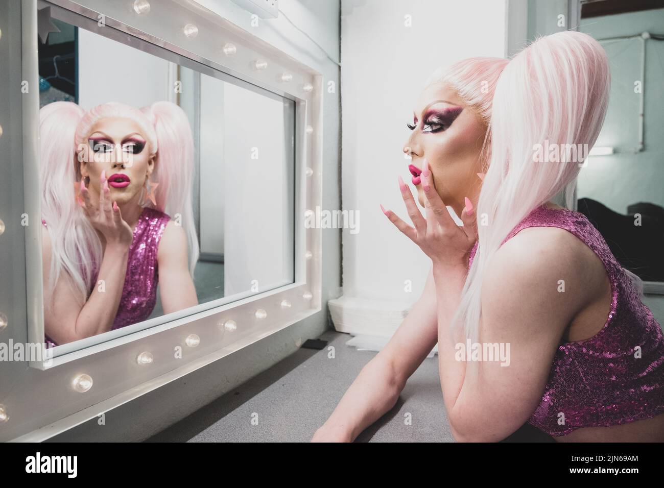 Personne non binaire appliquant faire glisser Reine maquillage Backstage, regardant dans miroir Banque D'Images