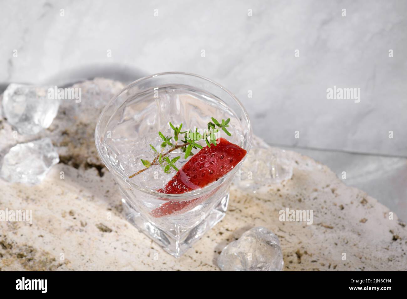 Vodka en verre à feu avec glace, décorée de tranches de fraise et de thym sur le podium de travertin sur fond de marbre rose. Boisson alcoolisée cocktail Wi Banque D'Images