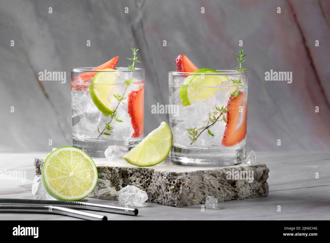 Mojito, margarita, daiquiri. Deux verres avec soda aux fraises fraîches, glace, citron vert, thym sur le podium en travertin sur pi Banque D'Images
