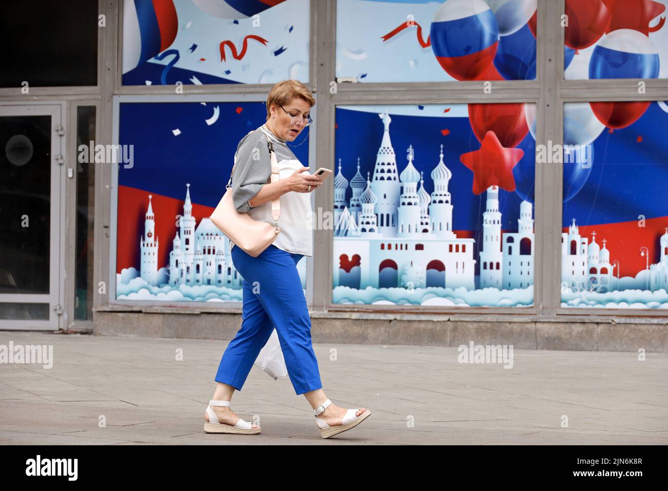 Femme surprise avec un smartphone marchant sur la rue de la ville sur fond de mur décoré pour l'anniversaire de Moscou Banque D'Images