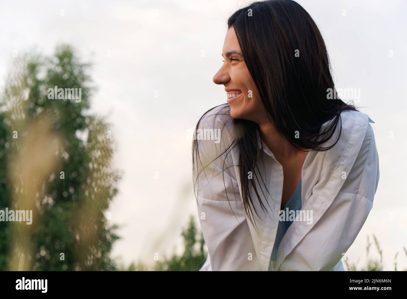 Jeune femme souriante en chemise blanche en pleine nature, assise à Meadow Banque D'Images