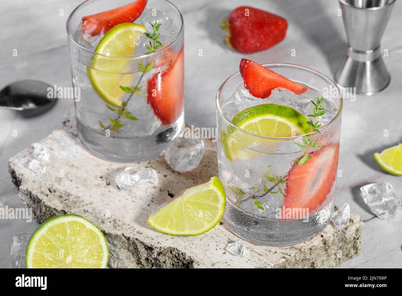 Mojito, margarita, daiquiri. Deux verres avec boisson fraîche au soda aux fraises, glace et outils barman sur le podiu de travertin Banque D'Images