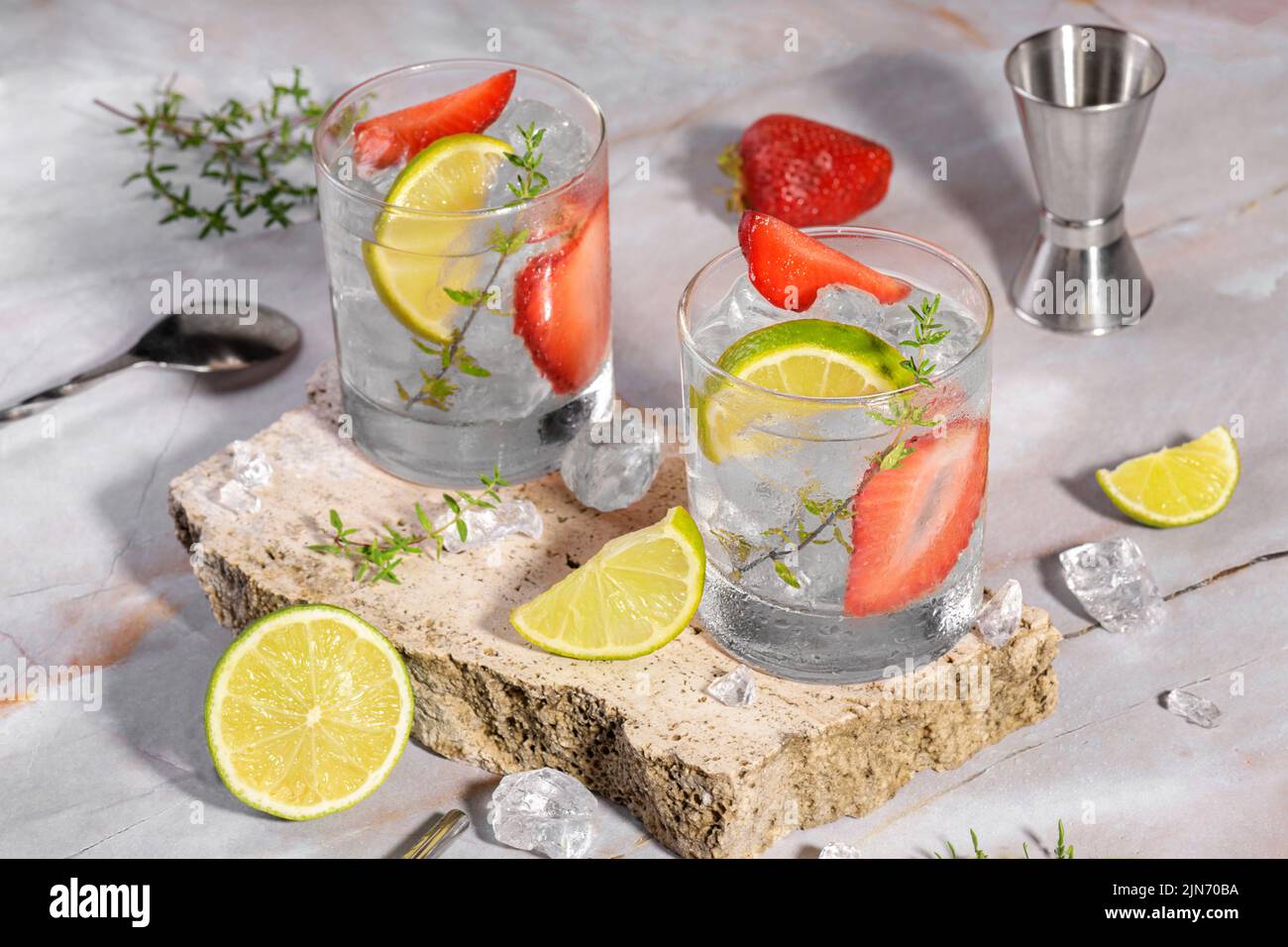 Mojito, margarita, daiquiri. Deux verres avec boisson fraîche au soda aux fraises, glace et outils barman sur le podiu de travertin Banque D'Images