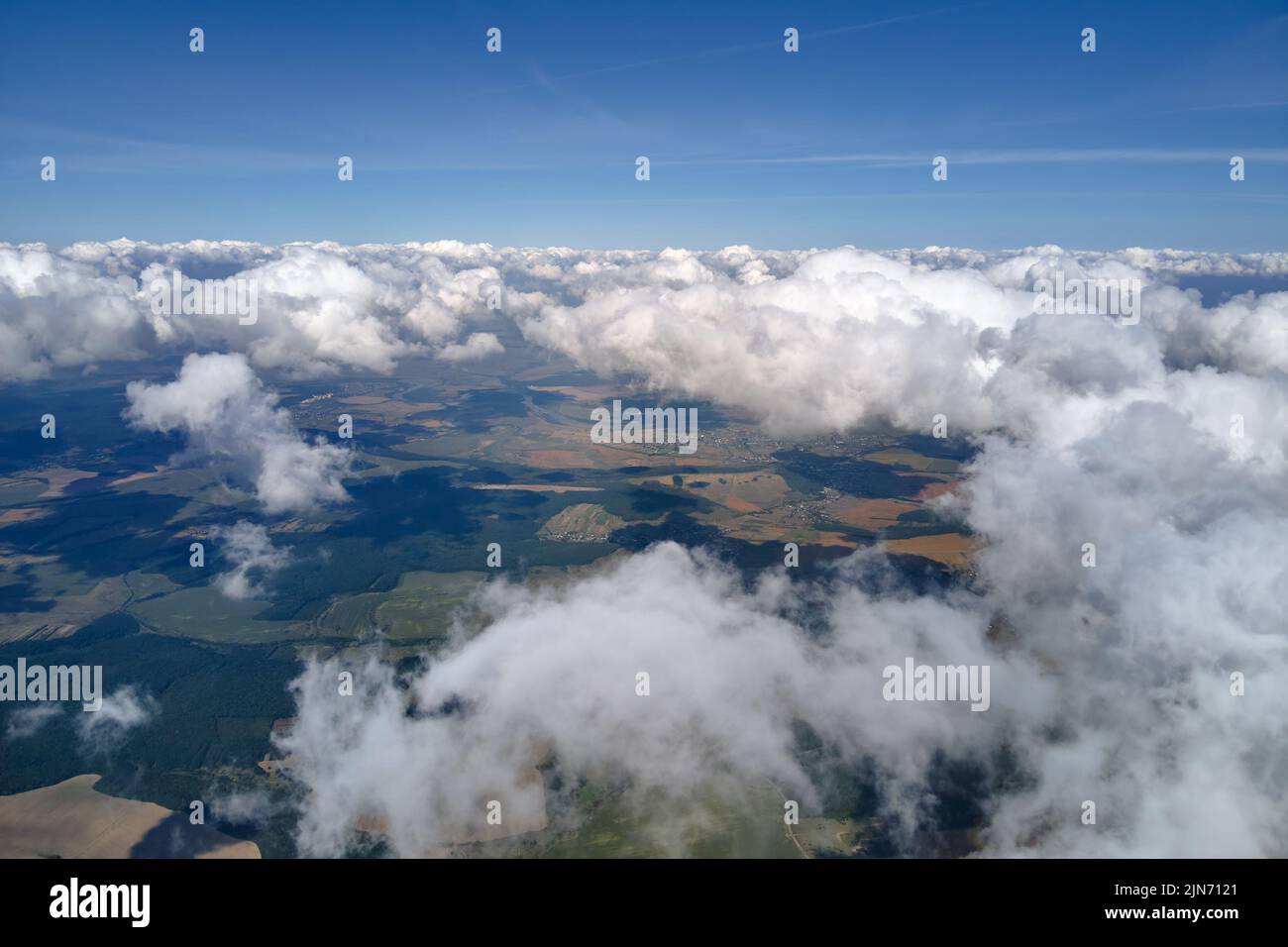 Vue aérienne depuis la fenêtre de l'avion à haute altitude de la terre couverte de cumulus bouffieux qui se forment avant la tempête Banque D'Images