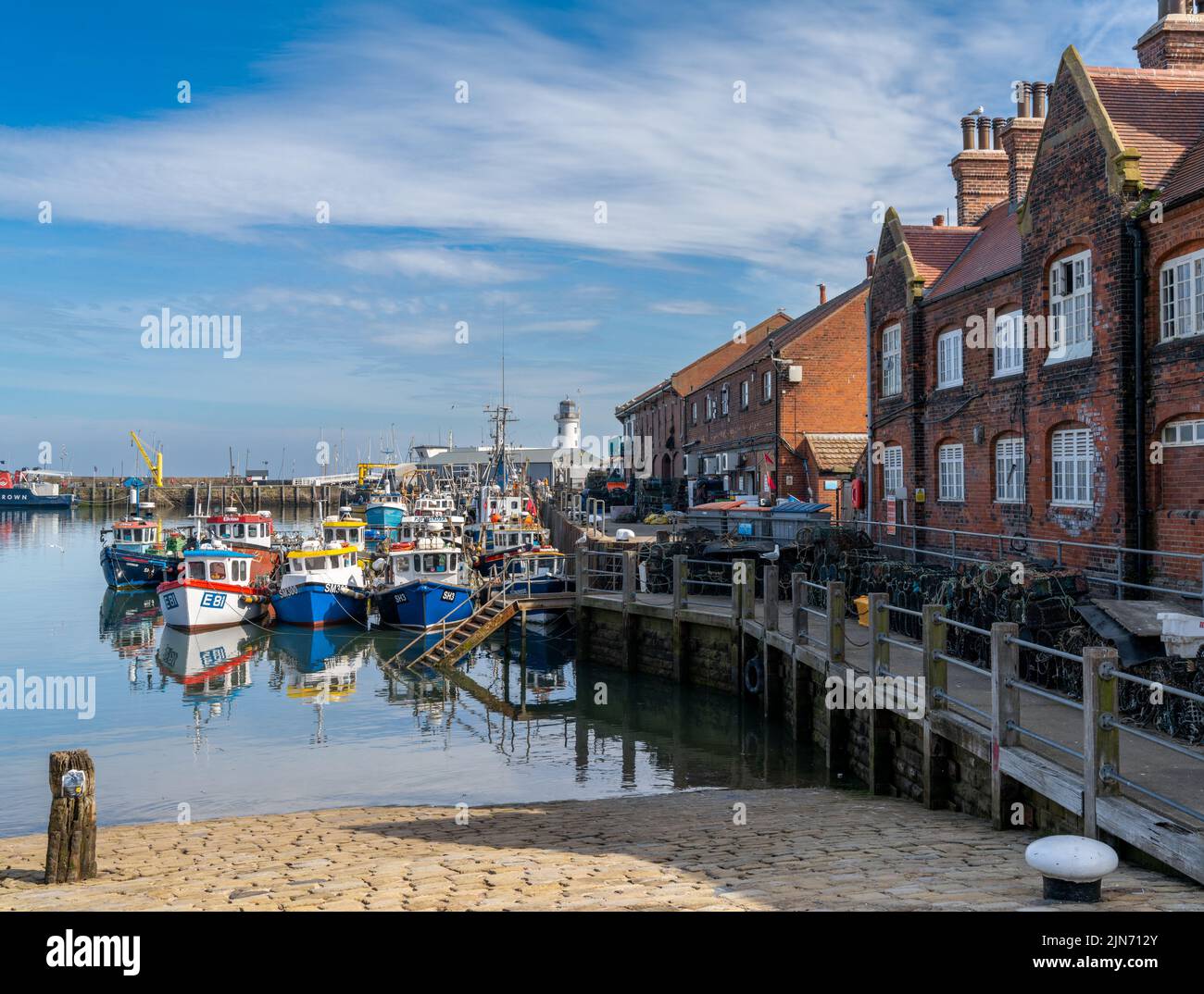 Scarborough, Royaume-Uni - 16 juin 2022 : bateaux de pêche et chalutiers colorés à côté du port en brique rouge de la marina et du port de Scarb Banque D'Images