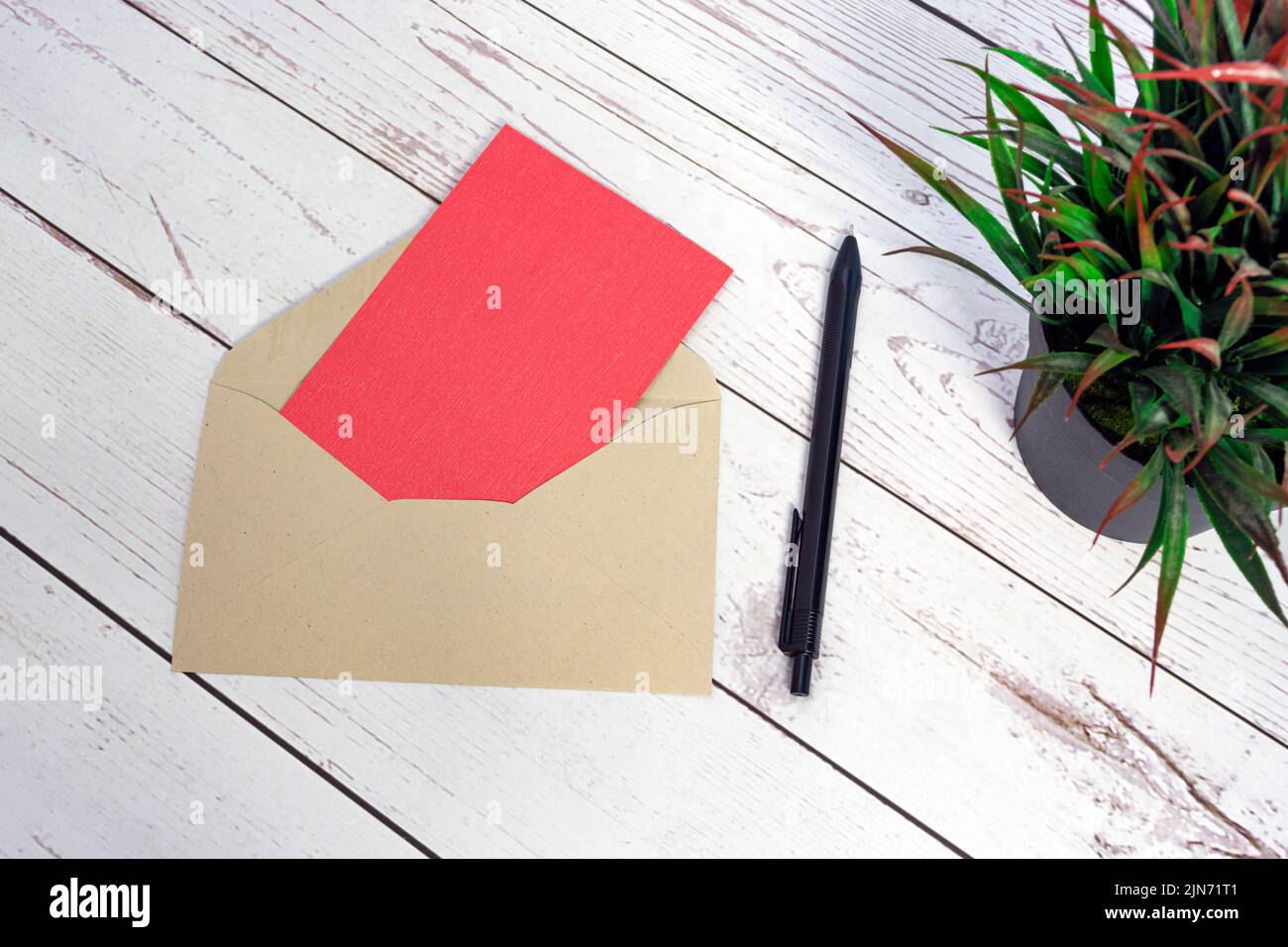 Maquette de carte rouge avec enveloppe, stylo et plante en pot sur table en bois. Banque D'Images
