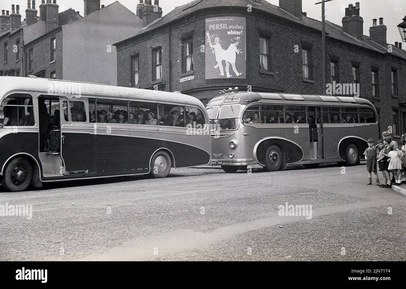 1950s, historique, excursion en autocar, Sheffield-Torquay Express. Les passagers assis à l'intérieur de deux cars de Littlewood Bros attendent sur Grimesthorpe Road devant le magasin d'angle de Lily Bell, Sheffield, South Yorkshire, Angleterre, Royaume-Uni. Banque D'Images