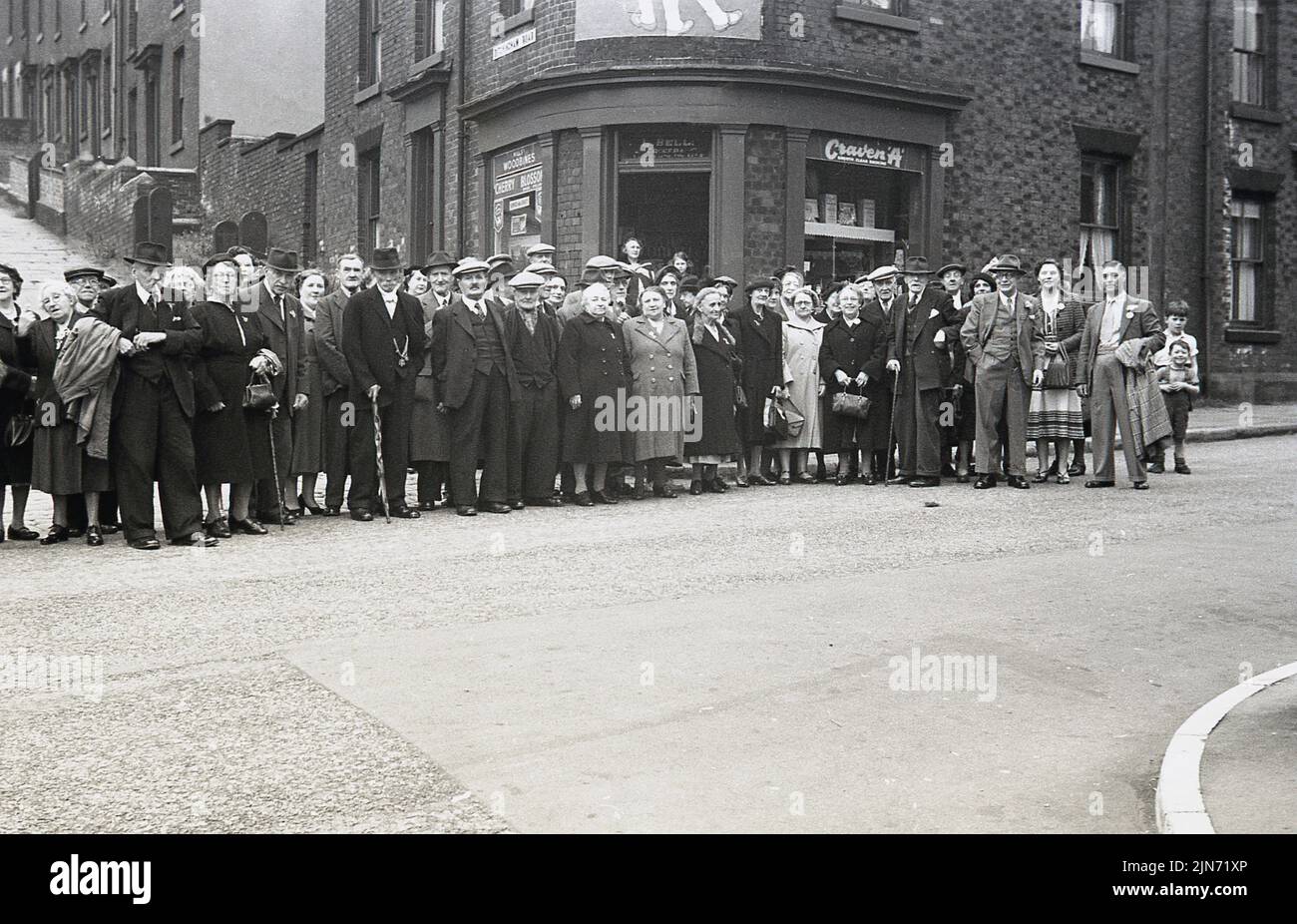 1950s, historique, voyage en autocar, Sheffield-Torquay Express, passagers masculins et féminins dans la rue de Grimesthorpe Rd, Pitsmoor à Sheffield, dans le Yorkshire du Sud, Angleterre, Royaume-Uni, Pour une photo de groupe avant le long voyage vers le sud jusqu'à la station balnéaire de Devon de Torquay. La plupart des hommes et certaines femmes portent des chapeaux. C'était une excursion de nuit, partant vendredi, arrivant à Torquay samedi matin, de retour à Sheffield dimanche. C'est une aventure pour les OAP ! Derrière eux, la colline escarpée de Ditchingham Road. Au coin de la rue, Lliy Bell's Grocery. Banque D'Images