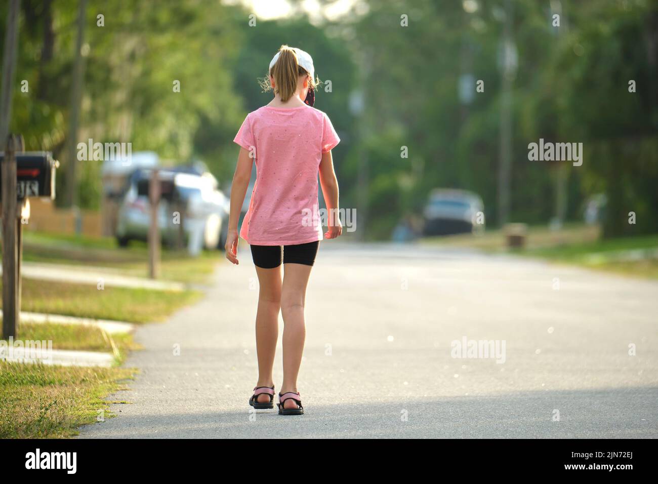 Vue arrière d'une jeune fille triste marchant seul le long de la rue verte le jour ensoleillé de l'été Banque D'Images