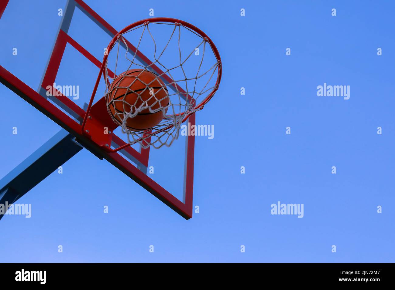 Un basket-ball dans un filet sur fond bleu ciel. La bille frappe l'anneau. Terrain de basket-ball extérieur. Le basket-ball a volé à travers l'anneau, volant à travers le panier et le filet. Banque D'Images