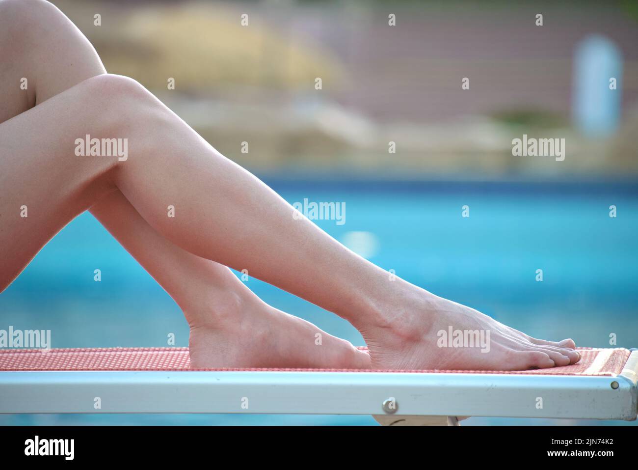 Fines jambes de femme dans une robe blanche courte se détendre près de la piscine, allongé sur une chaise longue. Concept de vacances d'été Banque D'Images