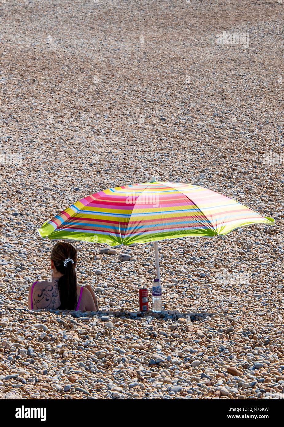 jeune femme assise sur la plage sous un parasol ou un parasol pendant une vague de chaleur un jour d'été ensoleillé à l'ombre du soleil, dame sur la plage avec parasol. Banque D'Images