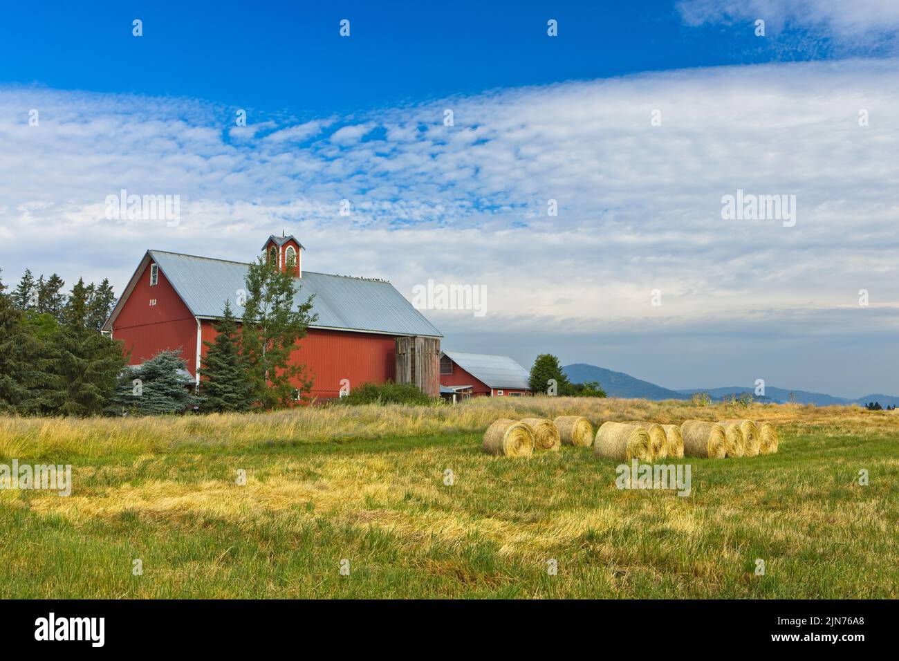 Une grange rouge se tient près d'un champ avec des balles de foin dans le nord de l'Idaho. Banque D'Images