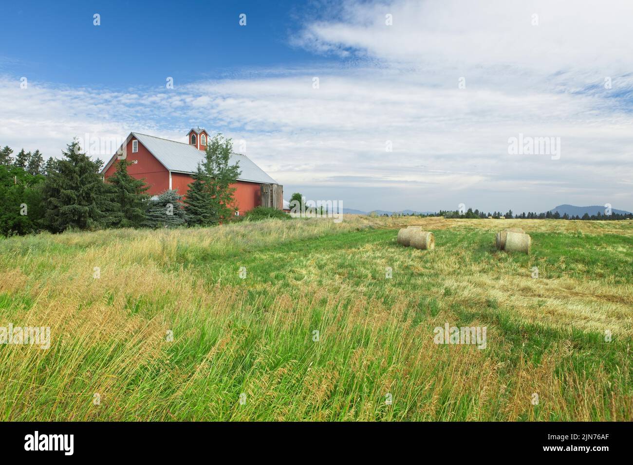 Une grange rouge se tient près d'un champ avec des balles de foin dans le nord de l'Idaho. Banque D'Images