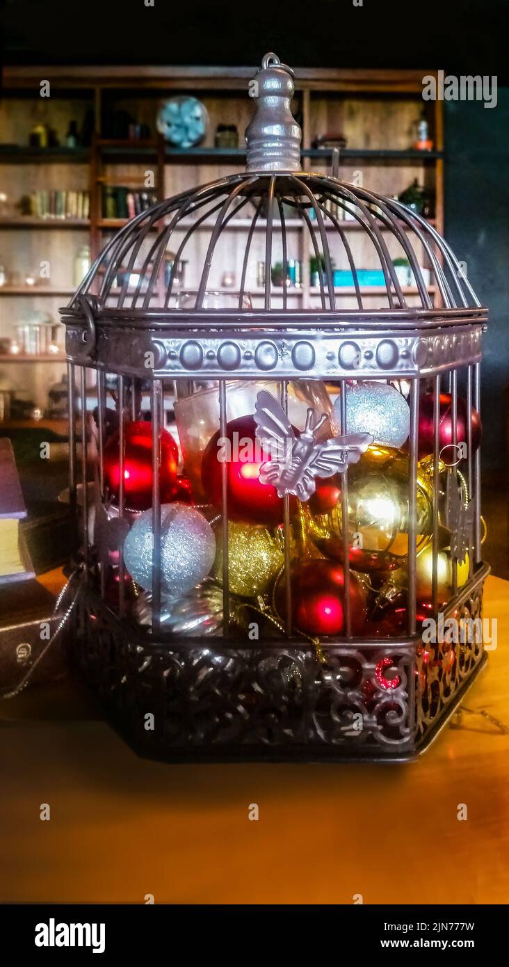 Cage métallique et métallique pleine d'ornements et de lumières de Noël sur un fond sombre de pièce floue avec des étagères et à côté des livres sur une table Banque D'Images