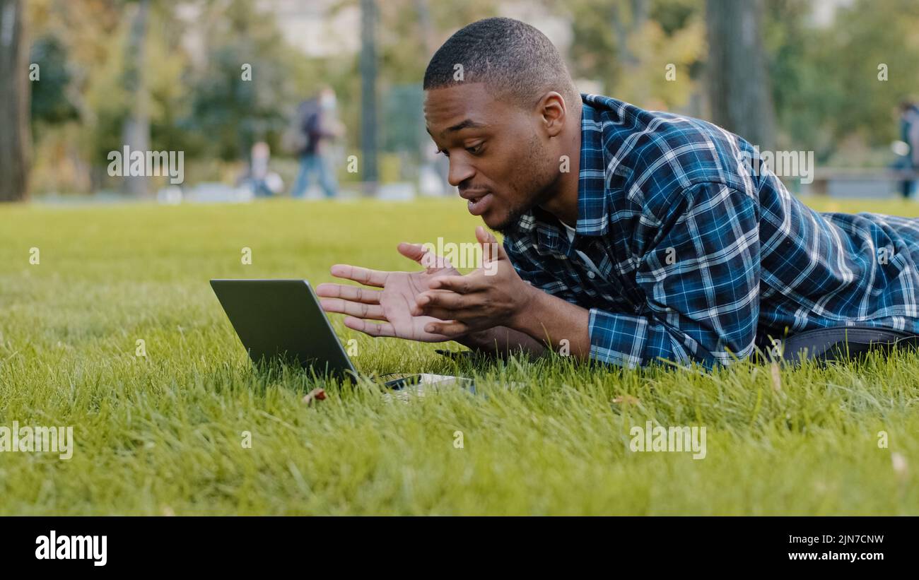 Afro-américain gars jeune homme d'affaires utilisateur couché sur pelouse verte dans le parc à l'aide d'un ordinateur portable en ligne appel conférence chat à distance conversation Banque D'Images