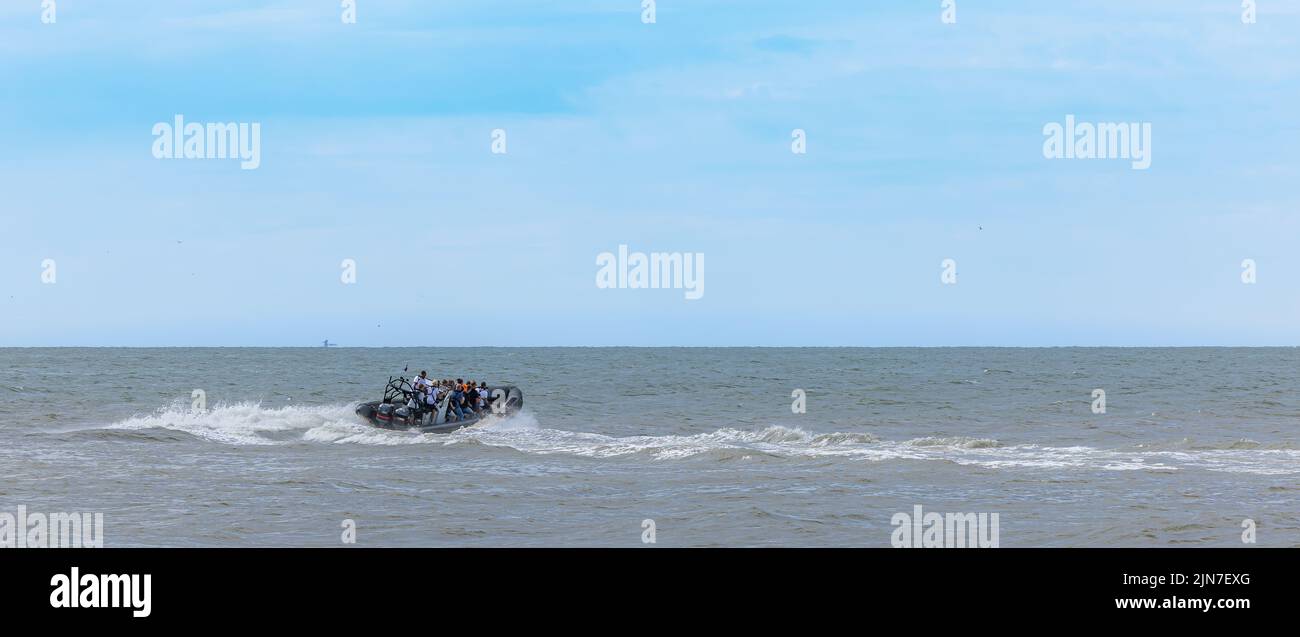 Hors-bord avec les touristes naviguant sur la mer ondulée bleue par une journée ensoleillée Banque D'Images