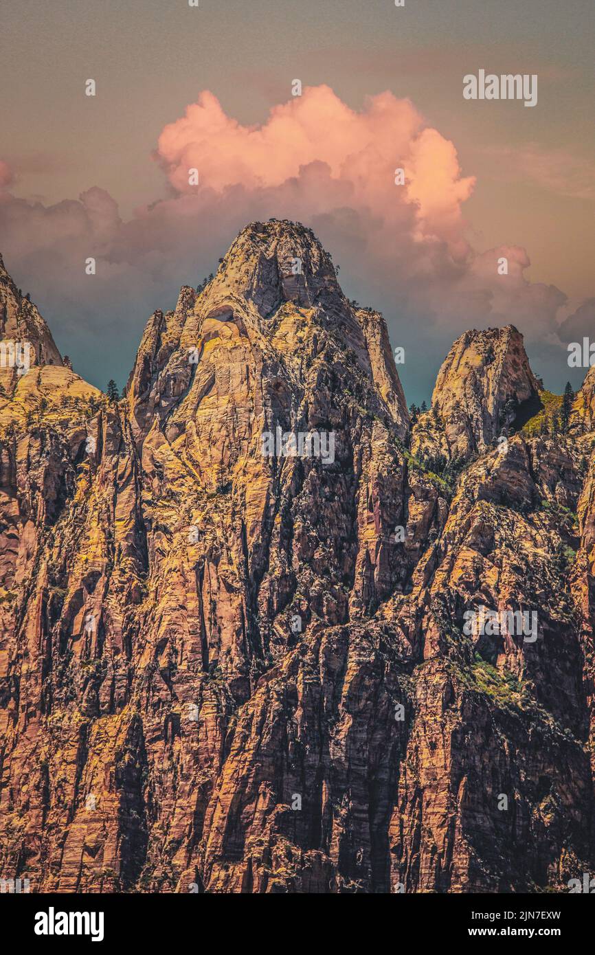 Des sommets imposants dans les badlands de l'Utah au crépuscule avec des nuages roses sur des falaises rocheuses arides et des arbres à ragoût minuscules au loin, accrochant aux rêves. Banque D'Images