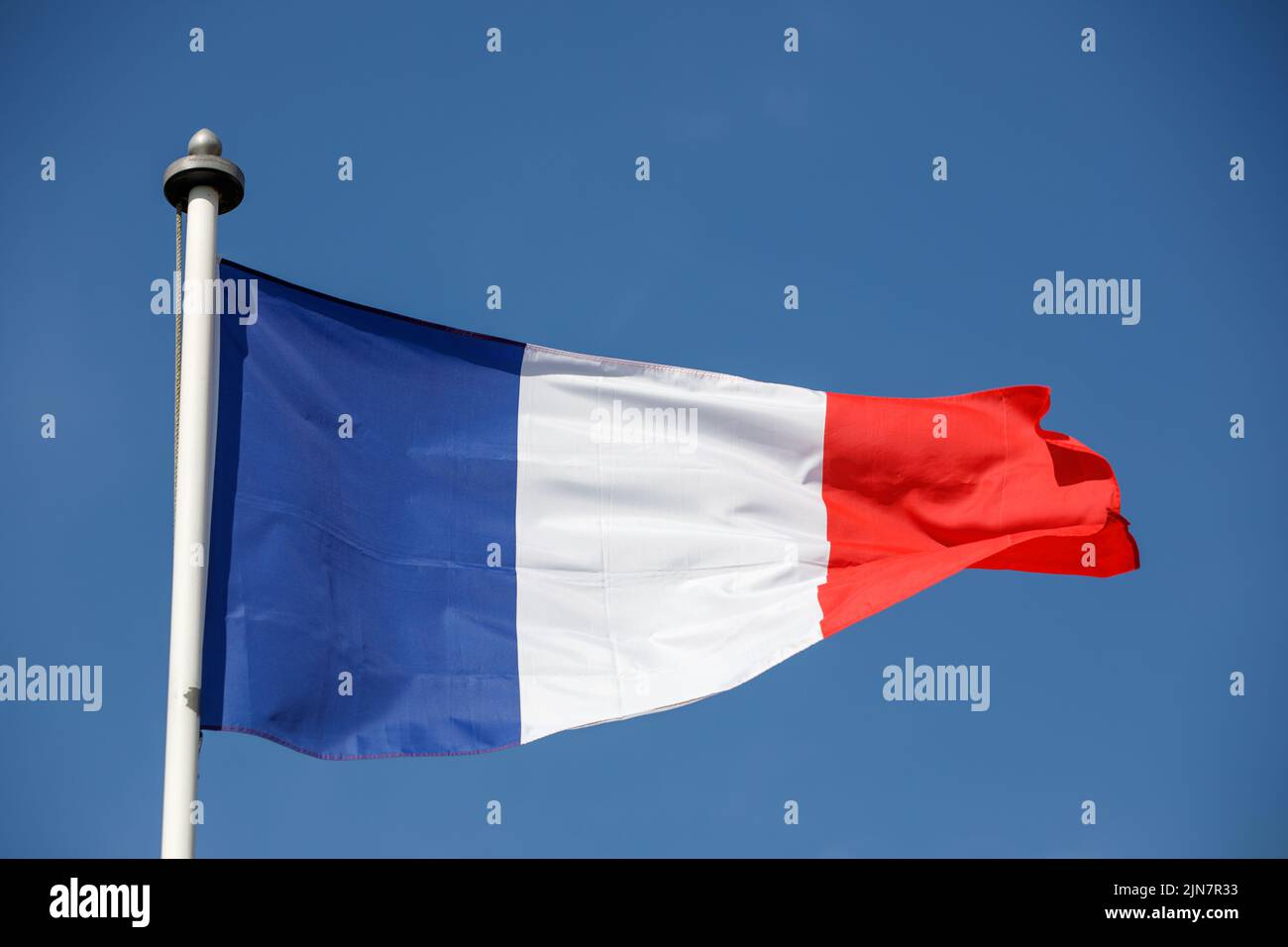 Drapeau français flottant dans le vent avec fond bleu ciel. Tricolore sur un mât blanc Banque D'Images