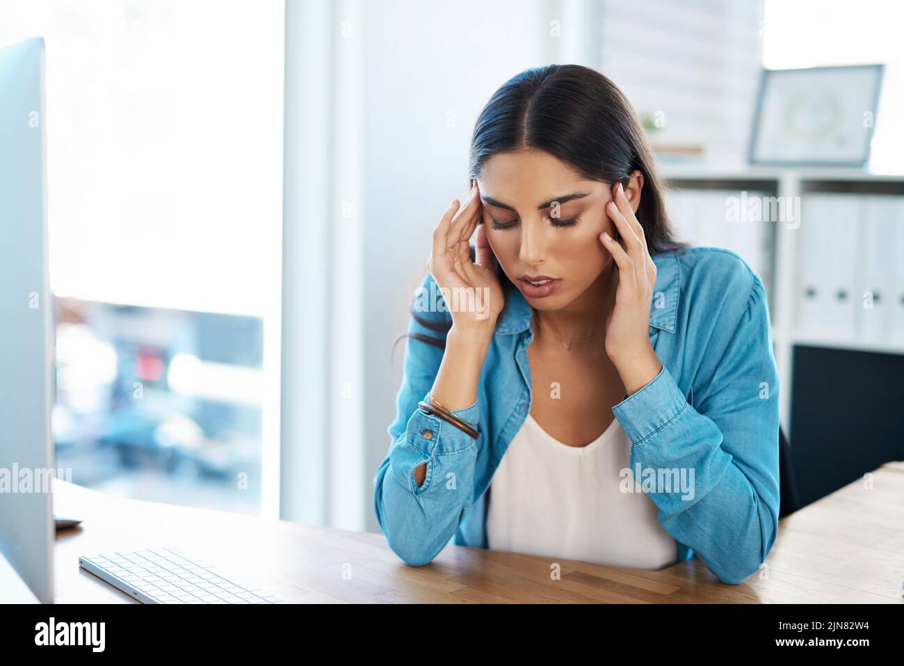 Voici que la tension tenace maux de tête de nouveau. Une jeune femme d'affaires regardant stressé dehors tout en travaillant dans un bureau. Banque D'Images