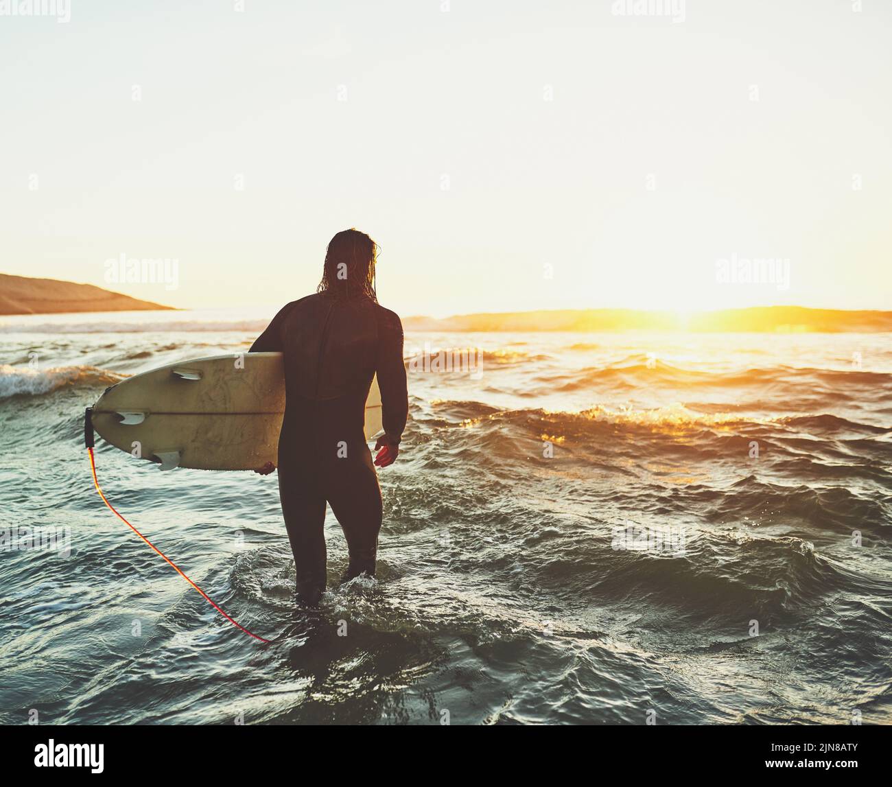 Le surf est le meilleur moyen de se sentir jeune, sauvage et libre. Vue arrière d'un jeune homme portant une planche de surf à la plage. Banque D'Images