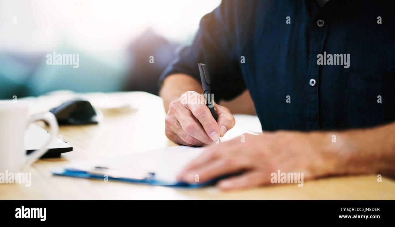En prenant tous les détails importants, un homme d'affaires méconnaissable écrit quelques notes sur un presse-papiers dans son bureau. Banque D'Images