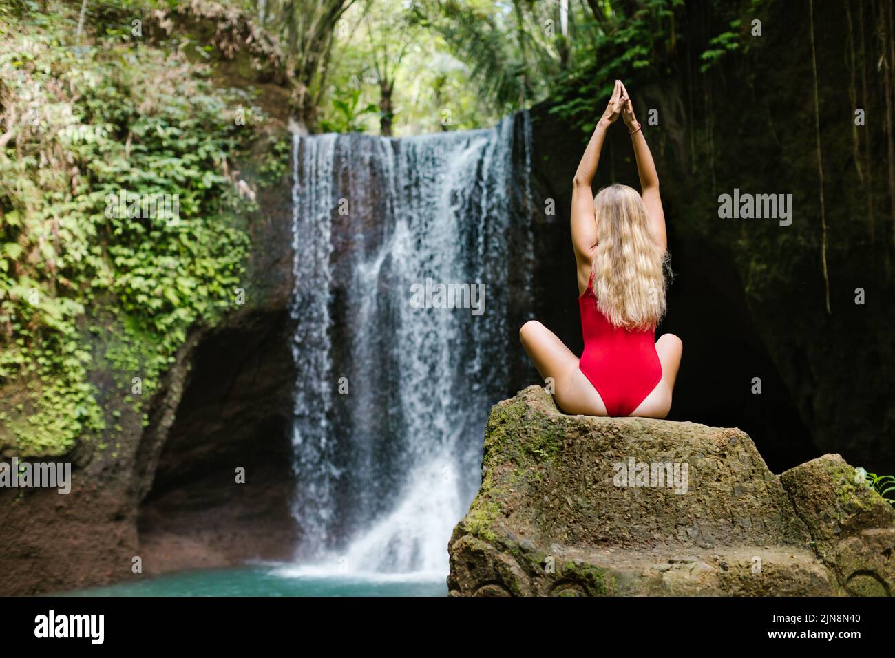 Femme en bikini assis sur le rocher, méditant dans le yoga pose sous l'eau tombant de Suwat cascade dans la jungle tropicale. Excursion d'une journée dans la nature, aventure en famille Banque D'Images