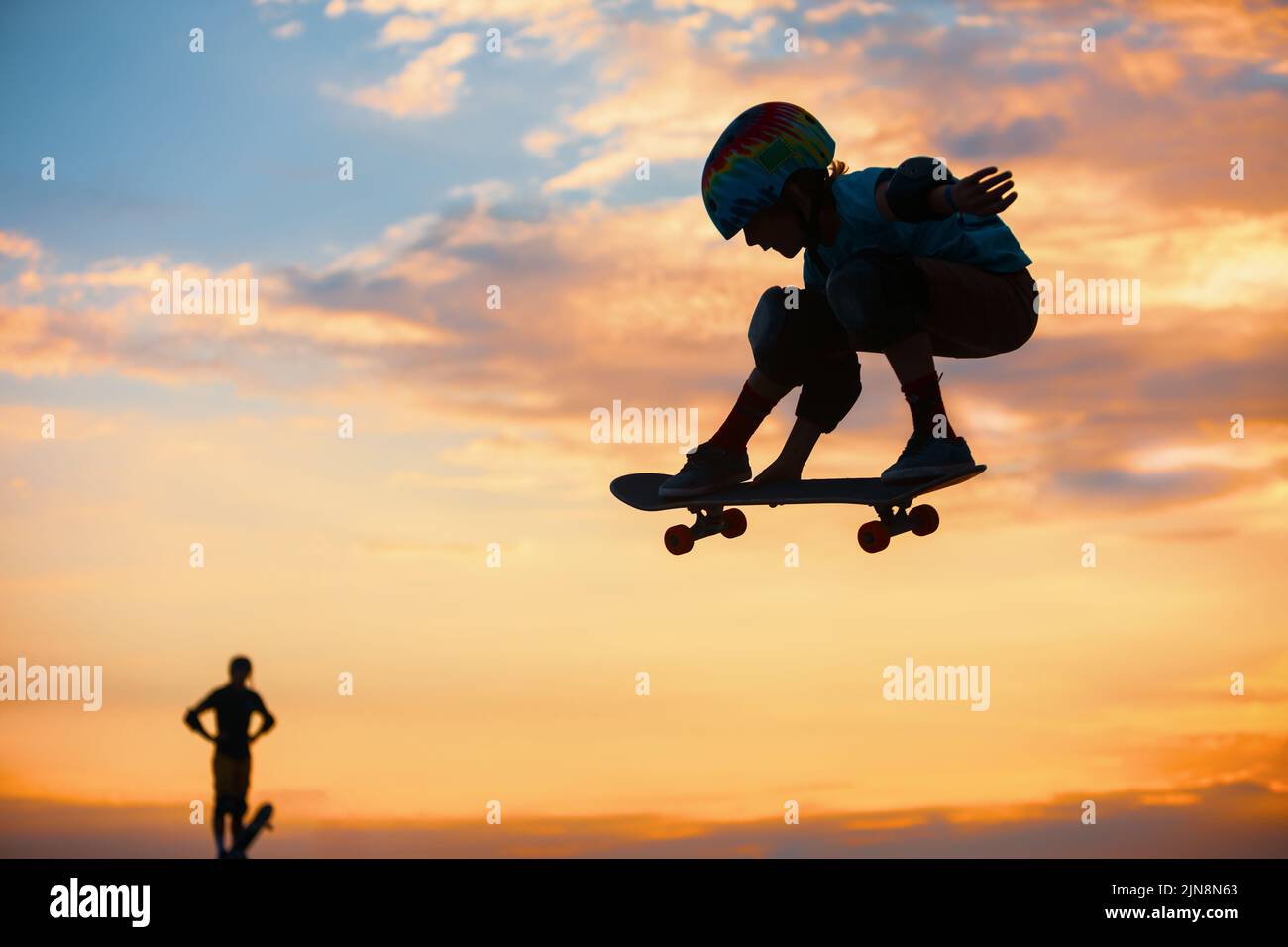 Skateboarder en action. Silhouette noire d'un jeune garçon faisant un tour d'air sur skate dans un skate Park sur fond de soleil. Culture de rue, skateboard Banque D'Images