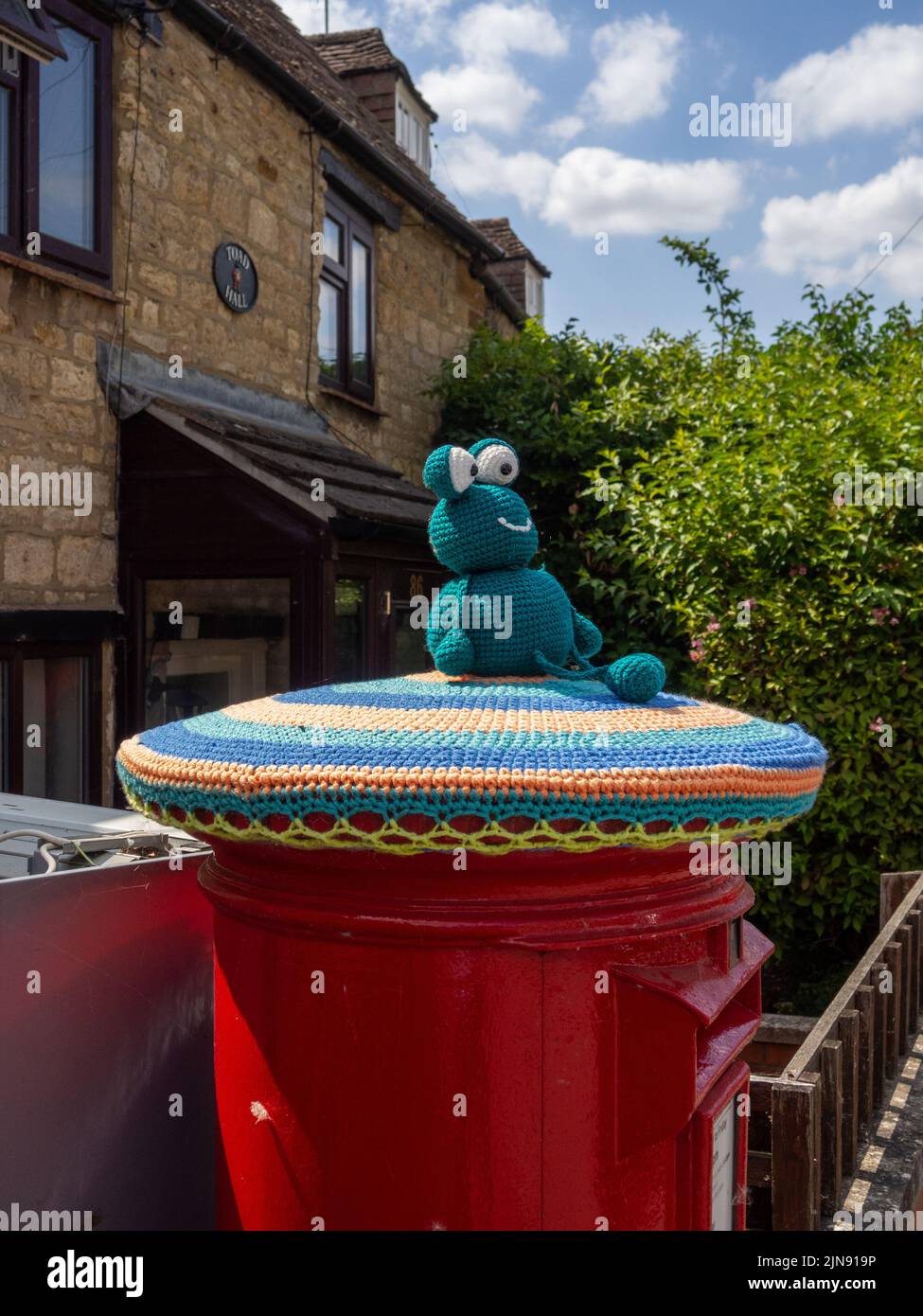 Boîte postale de Red Royal Mail surmontée d'une grenouille tricotée, ou d'un bombardement de fils, dans le village de Hackleton, dans le Northamptonshire, au Royaume-Uni Banque D'Images