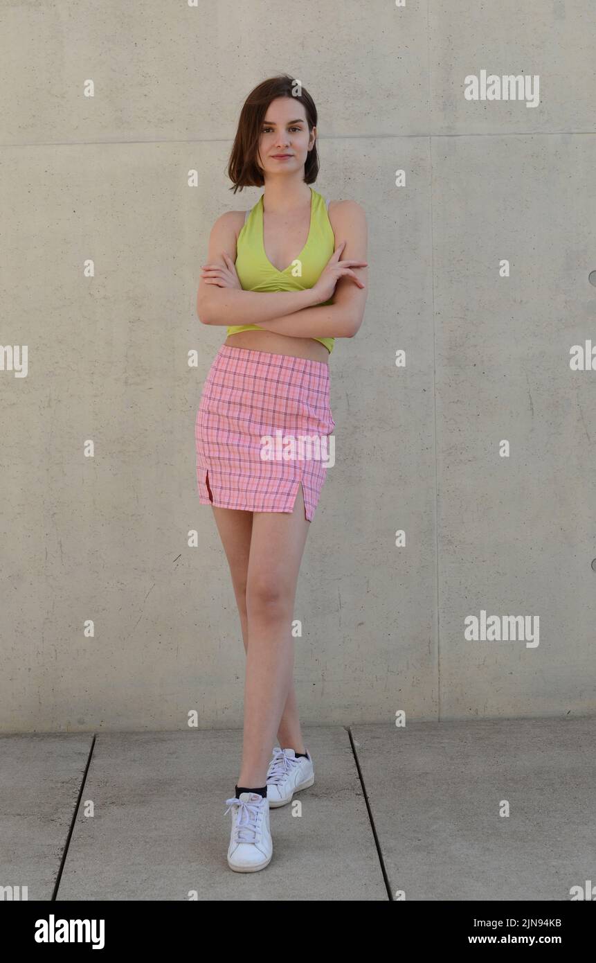 jeune fille de mode en minijupe rose et haut jaune reste devant un mur gris Banque D'Images