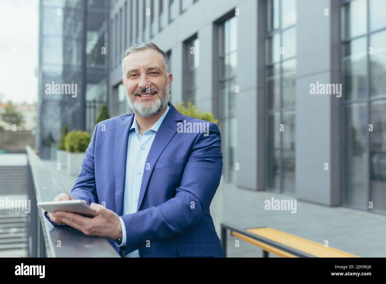 Portrait d'un patron d'homme d'affaires à cheveux gris, homme à l'extérieur du bureau utilisant un ordinateur tablette souriant et regardant l'appareil photo, investisseur en costume d'affaires, banquier heureux Banque D'Images