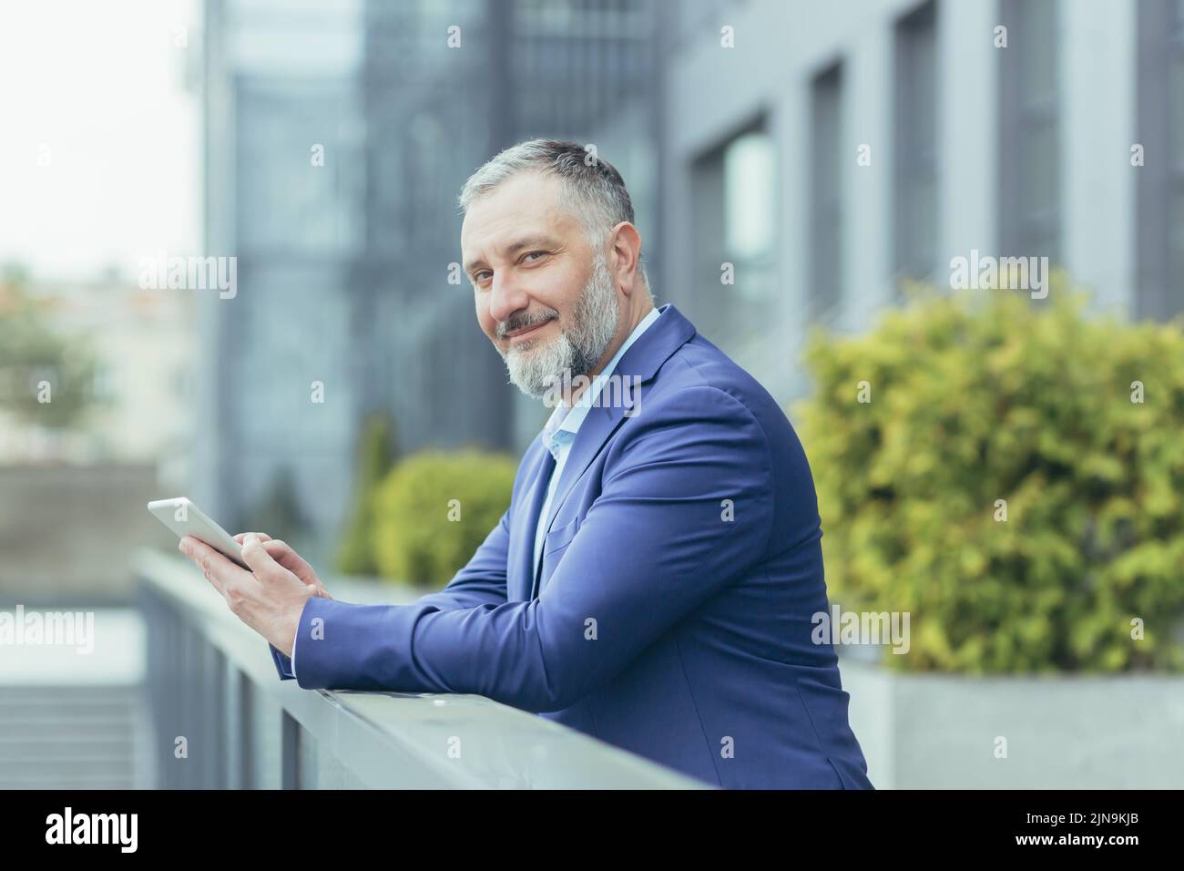 Portrait d'un patron d'homme d'affaires à cheveux gris, homme à l'extérieur du bureau utilisant un ordinateur tablette souriant et regardant l'appareil photo, investisseur en costume d'affaires, banquier heureux Banque D'Images