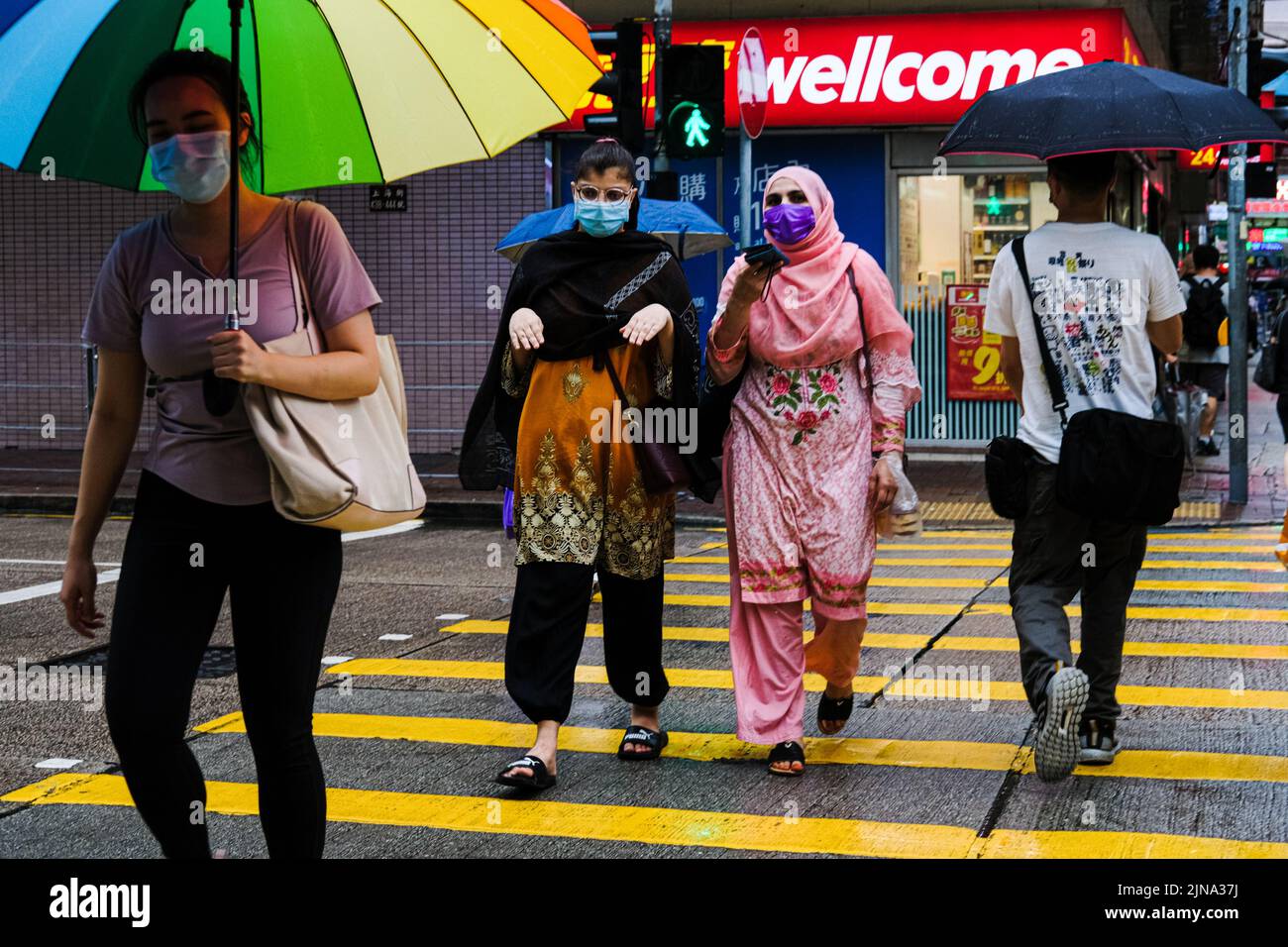 Hong Kong, Chine. 10th août 2022. Les gens portent un masque facial et des parasols traversent une rue sous la pluie. (Image de crédit : © Keith Tsuji/ZUMA Press Wire) Banque D'Images