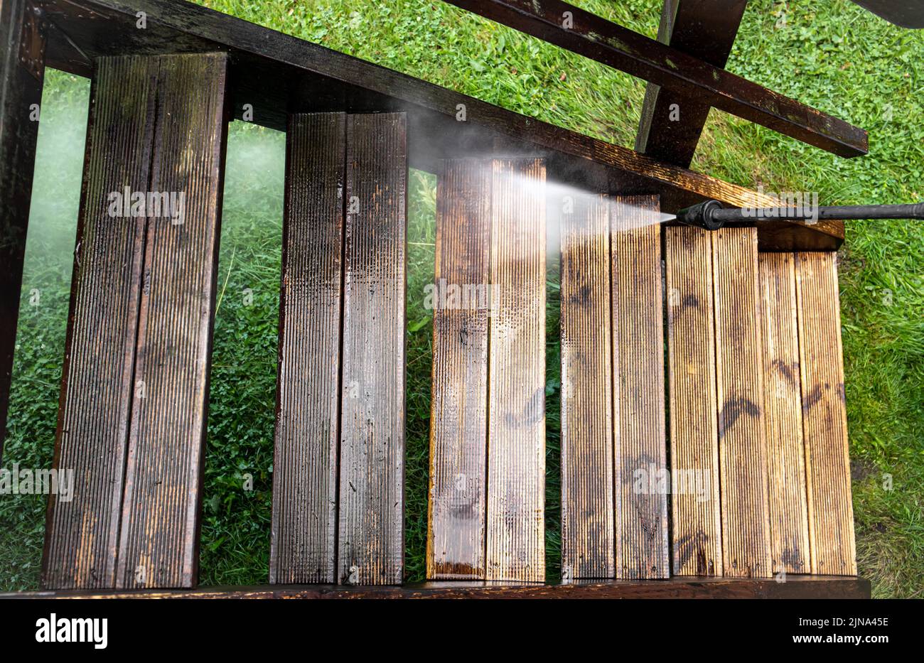 Vue rapprochée de l'utilisation d'un nettoyeur à pression pour nettoyer les escaliers en bois imprégné en terrasse à l'extérieur au printemps. Avant et après le nettoyage, grand contraste. Banque D'Images