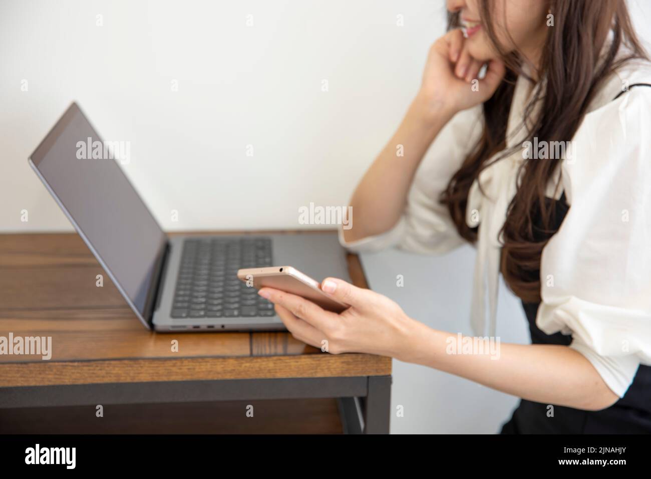 Une femme japonaise qui vérifie son smartphone dans la composition sans visage de son bureau à domicile Banque D'Images