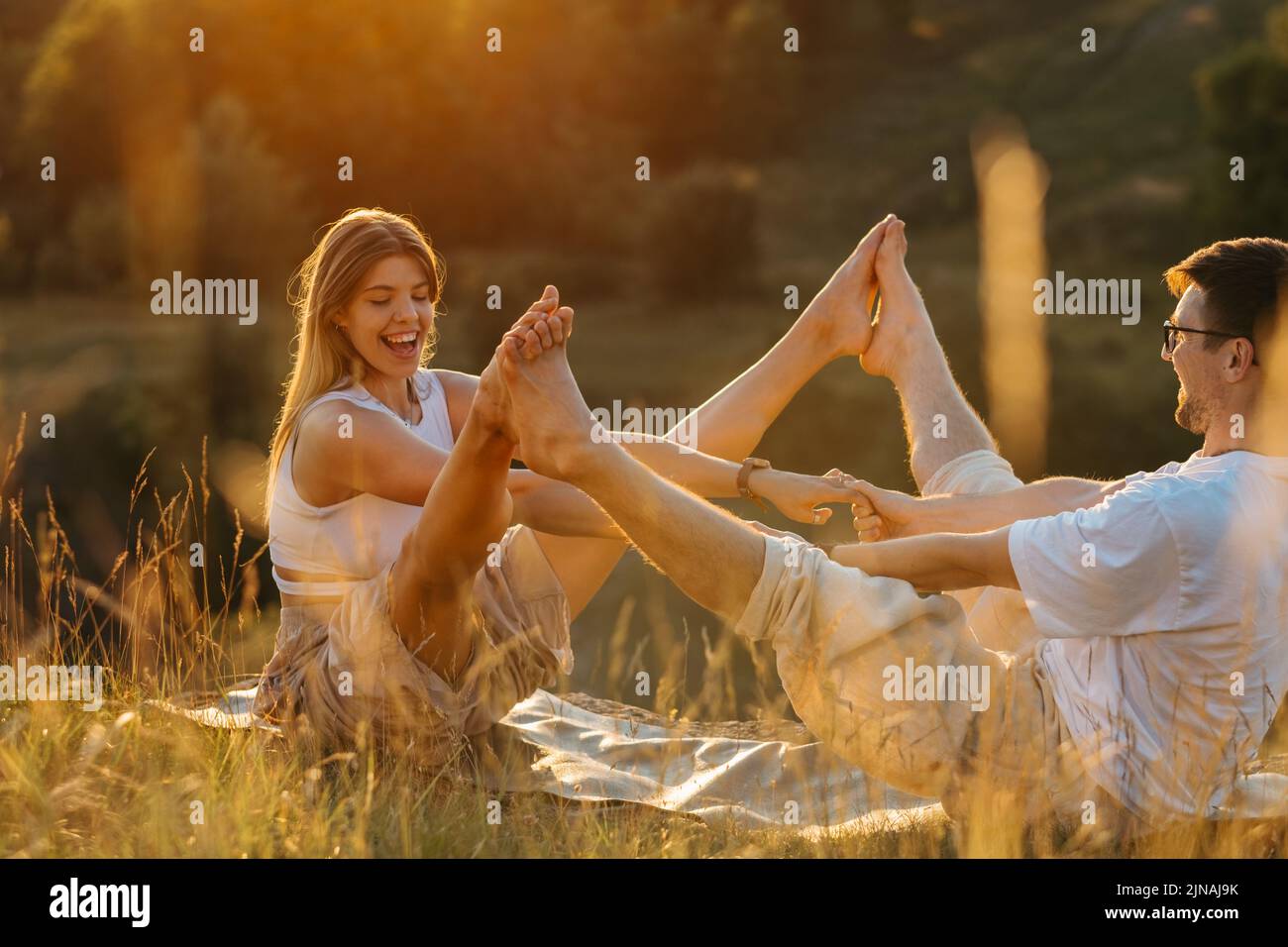 Jeune couple adulte pratiquant le yoga en plein air dans la nature, femme gaie et homme heureux faisant de l'exercice ensemble au coucher du soleil Banque D'Images