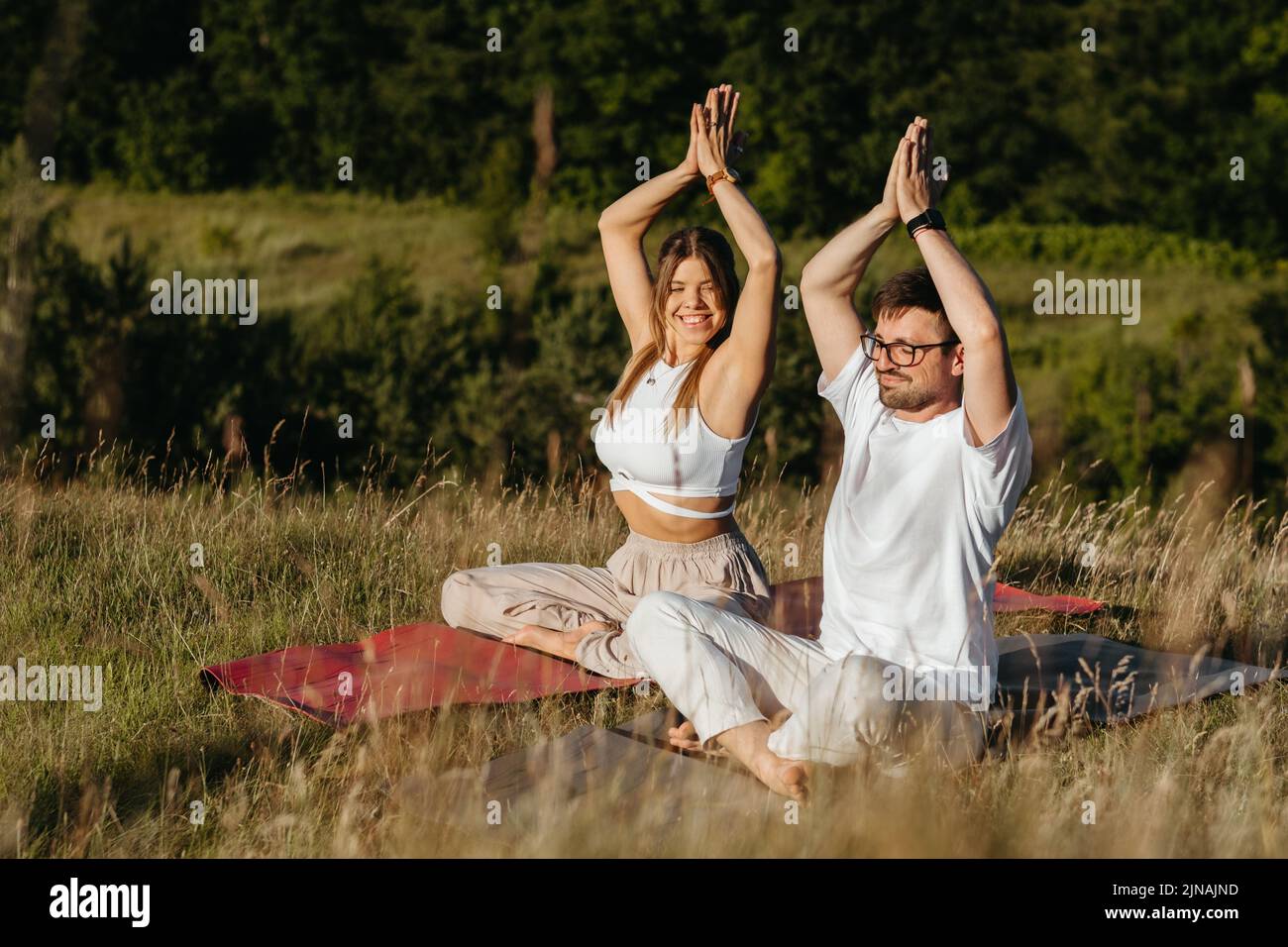 Femme gaie et homme heureux levant les mains au-dessus des têtes, jeune couple adulte méditant à l'extérieur dans la nature Banque D'Images