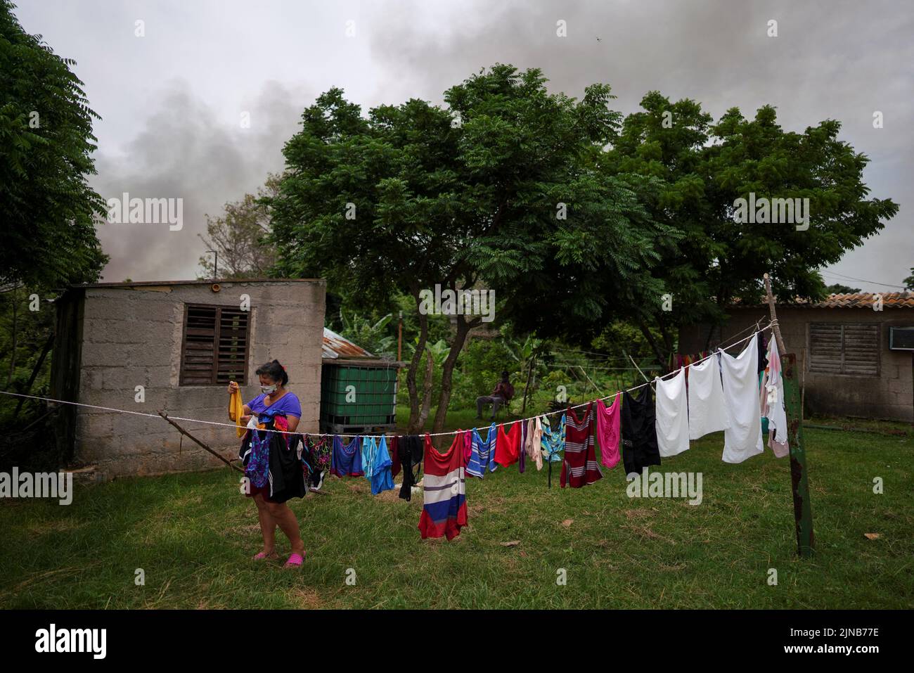 Adelaide Labradda, 60 ans, laisse sécher ses vêtements au milieu de la fumée provenant d'une zone détruite de chars qui ont explosé près du port de navires-citernes de Cuba à Matanzas, Cuba, 10 août 2022. REUTERS/Alexandre Meneghini Banque D'Images