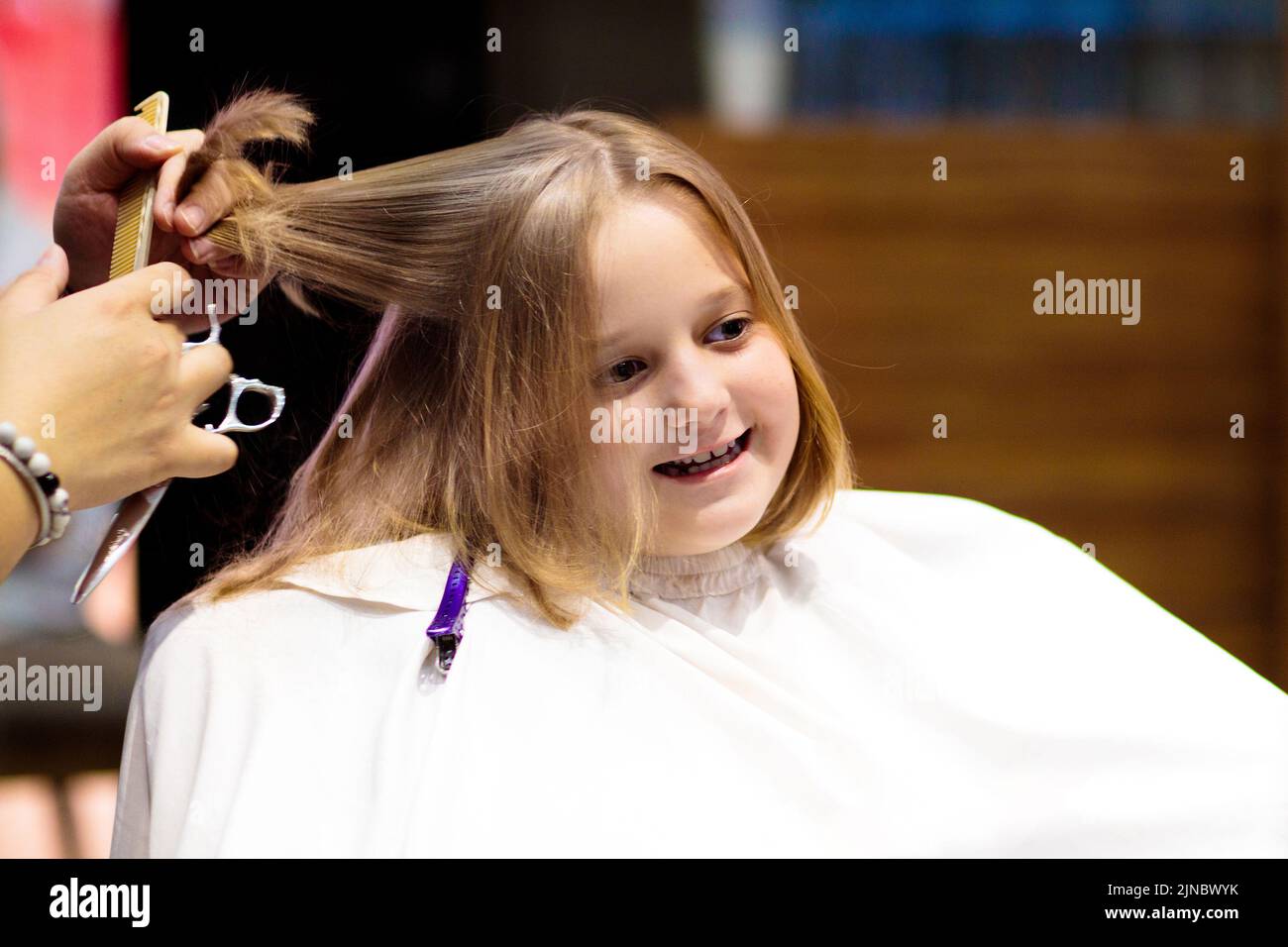 Enfant se découpent au salon de beauté. Coiffeur coupant les cheveux. Petite fille avec bob blond foncé à l'épaule chez le styliste. Spa pour enfants. Banque D'Images