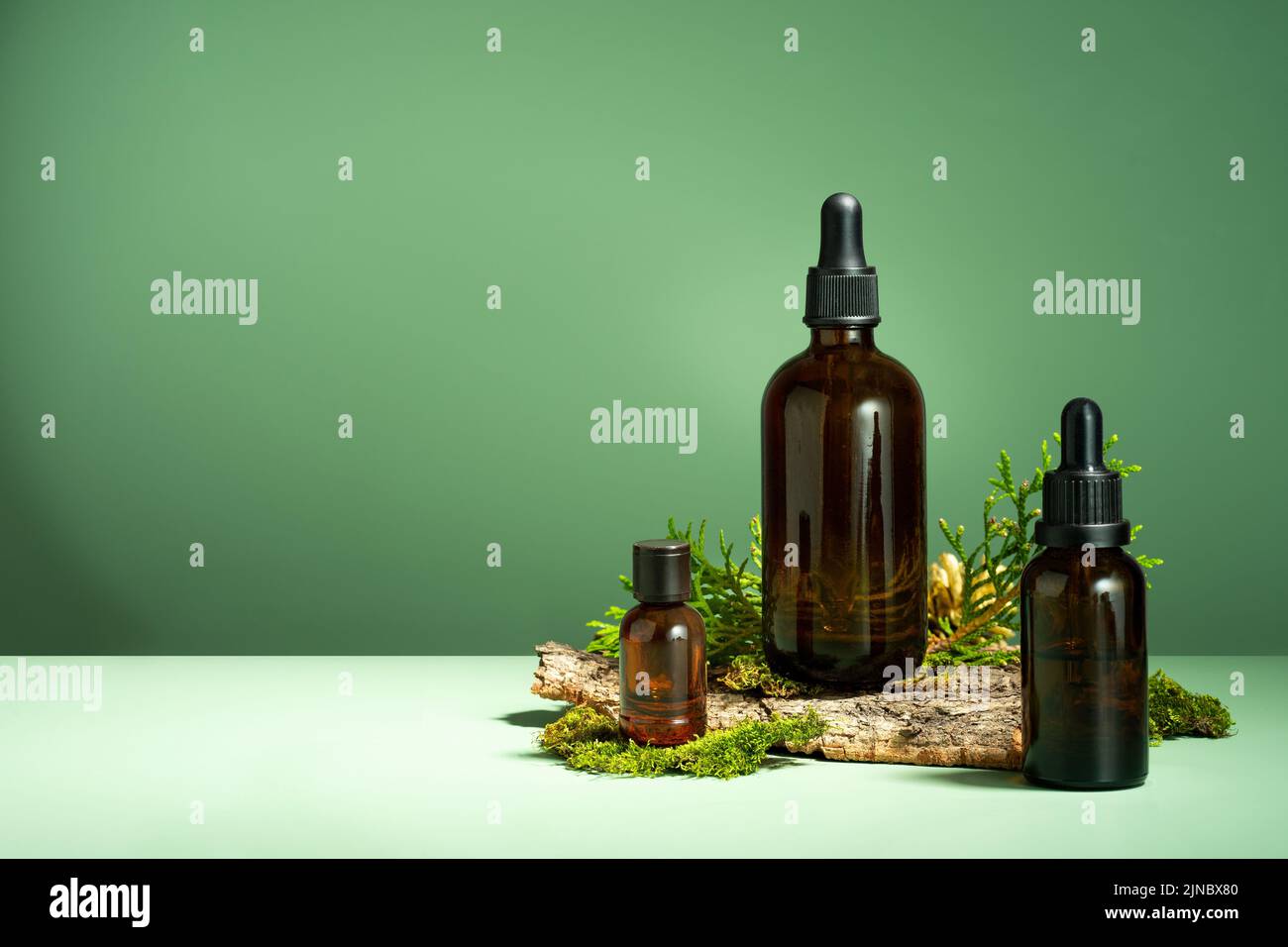 Un ensemble de bouteilles en verre marron, de mousse et d'écorce d'arbre sur fond vert. Huile avec du sérum pour les soins de la peau et des cheveux. Bouteille en verre d'huile essentielle pour le corps Banque D'Images