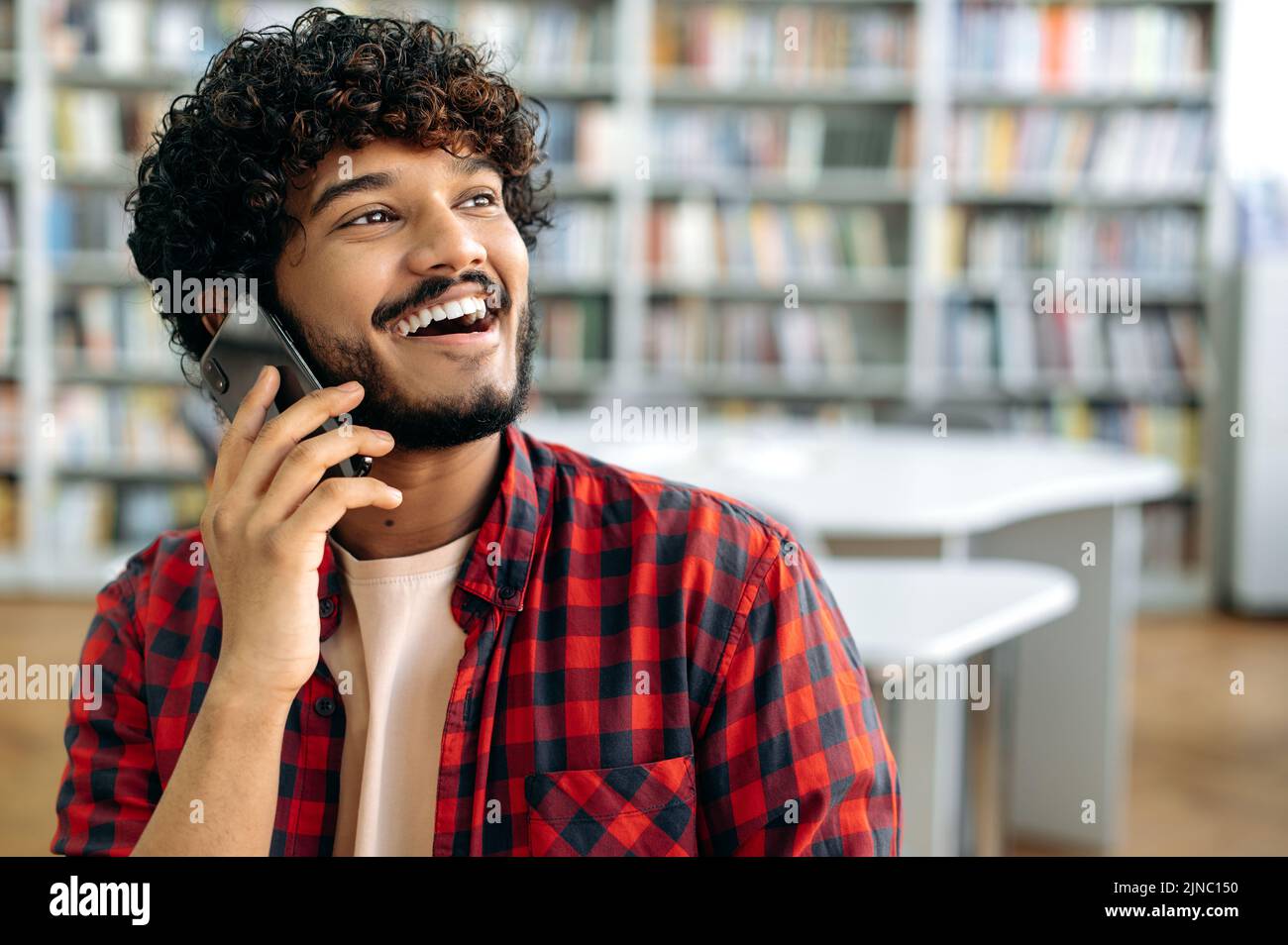 Conversation téléphonique. Gros plan d'un homme heureux aux cheveux bouclés et aux cheveux d'un indien ou d'un arabe, qui a négocié avec un smartphone, s'entretient avec un ami ou un collègue, regarde loin, souriant et amical Banque D'Images
